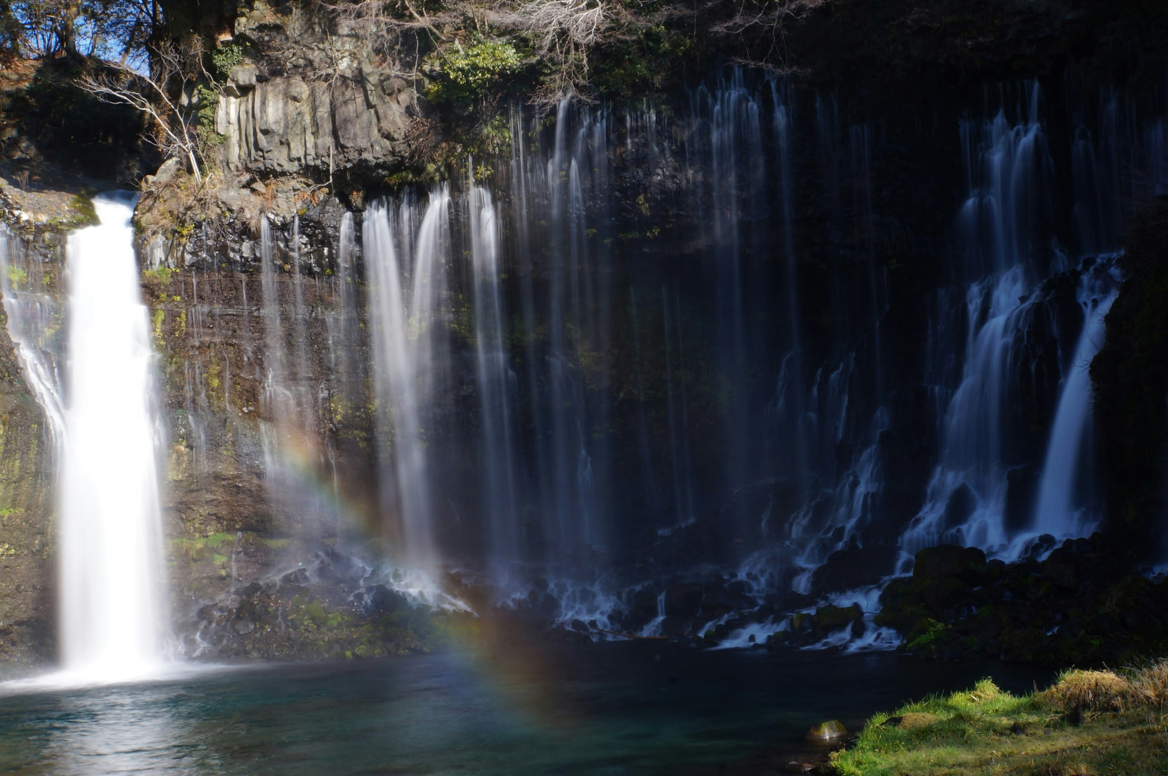 Belle cascade avec un arc-en-ciel au bord d'une eau tranquille