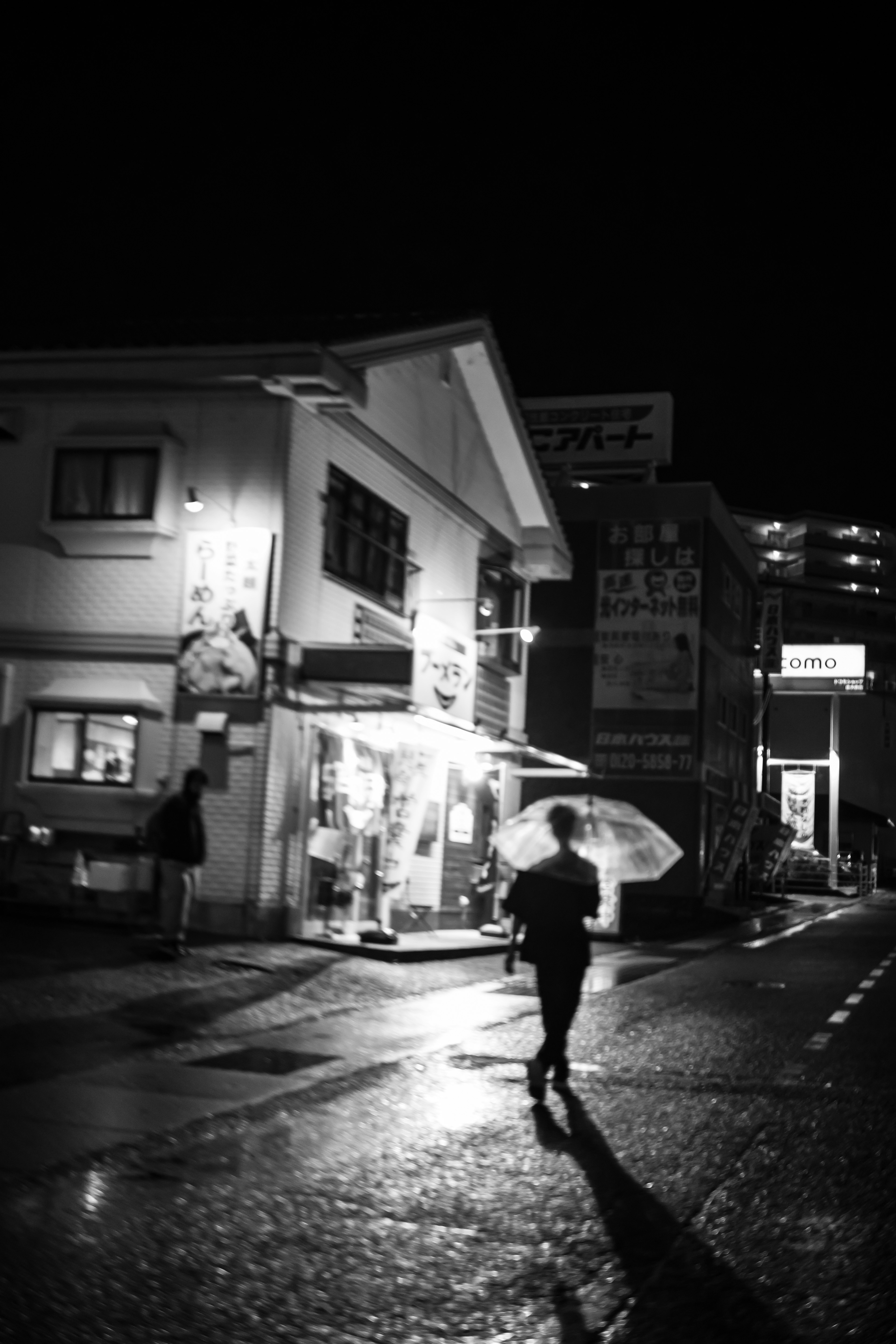 Black and white street scene at night with a person holding an umbrella