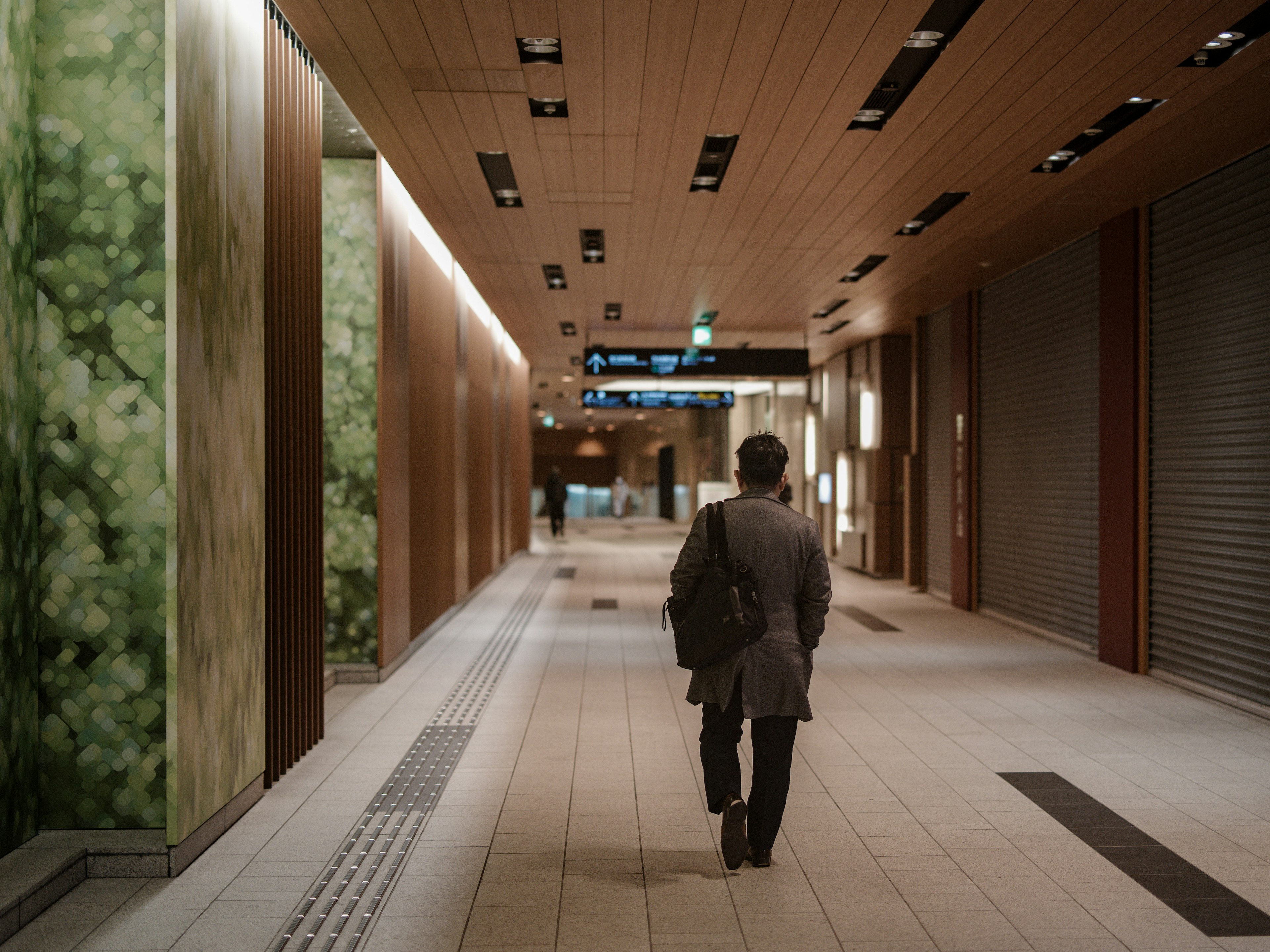 Businessman walking down a dimly lit corridor with green walls and wooden ceiling