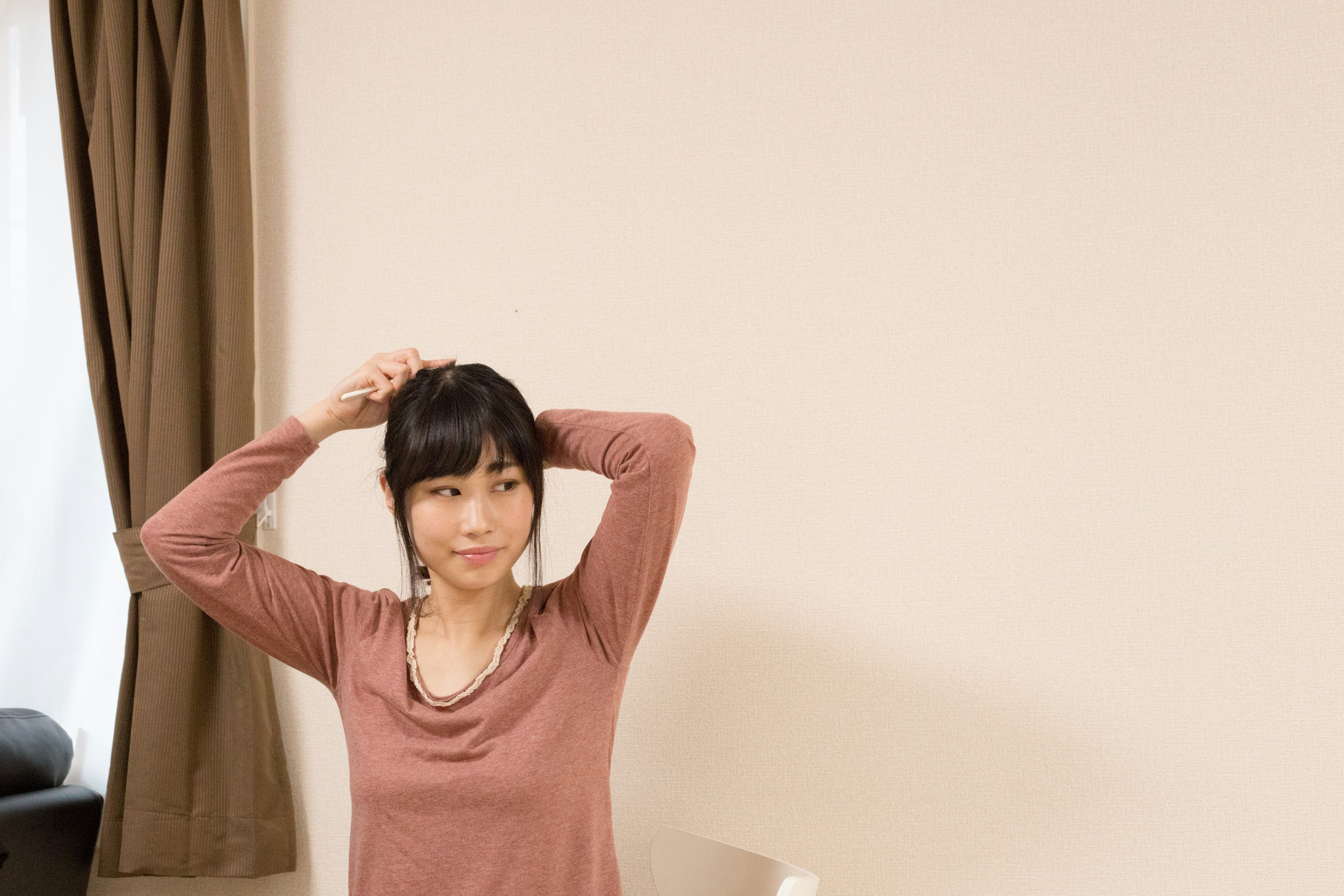 A woman styling her hair in a simple room with a neutral background