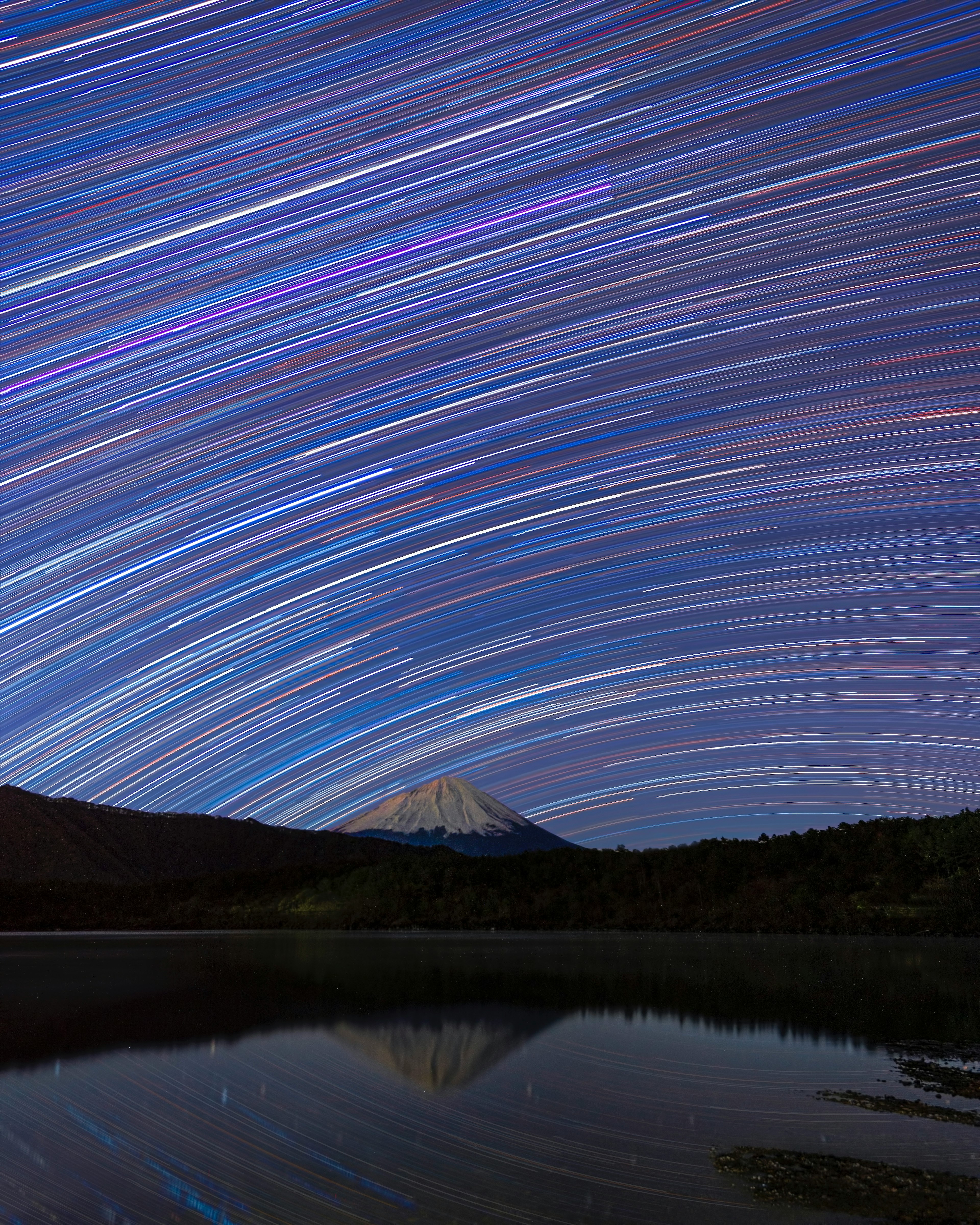 夜空中的星軌與寧靜湖面上的山的倒影