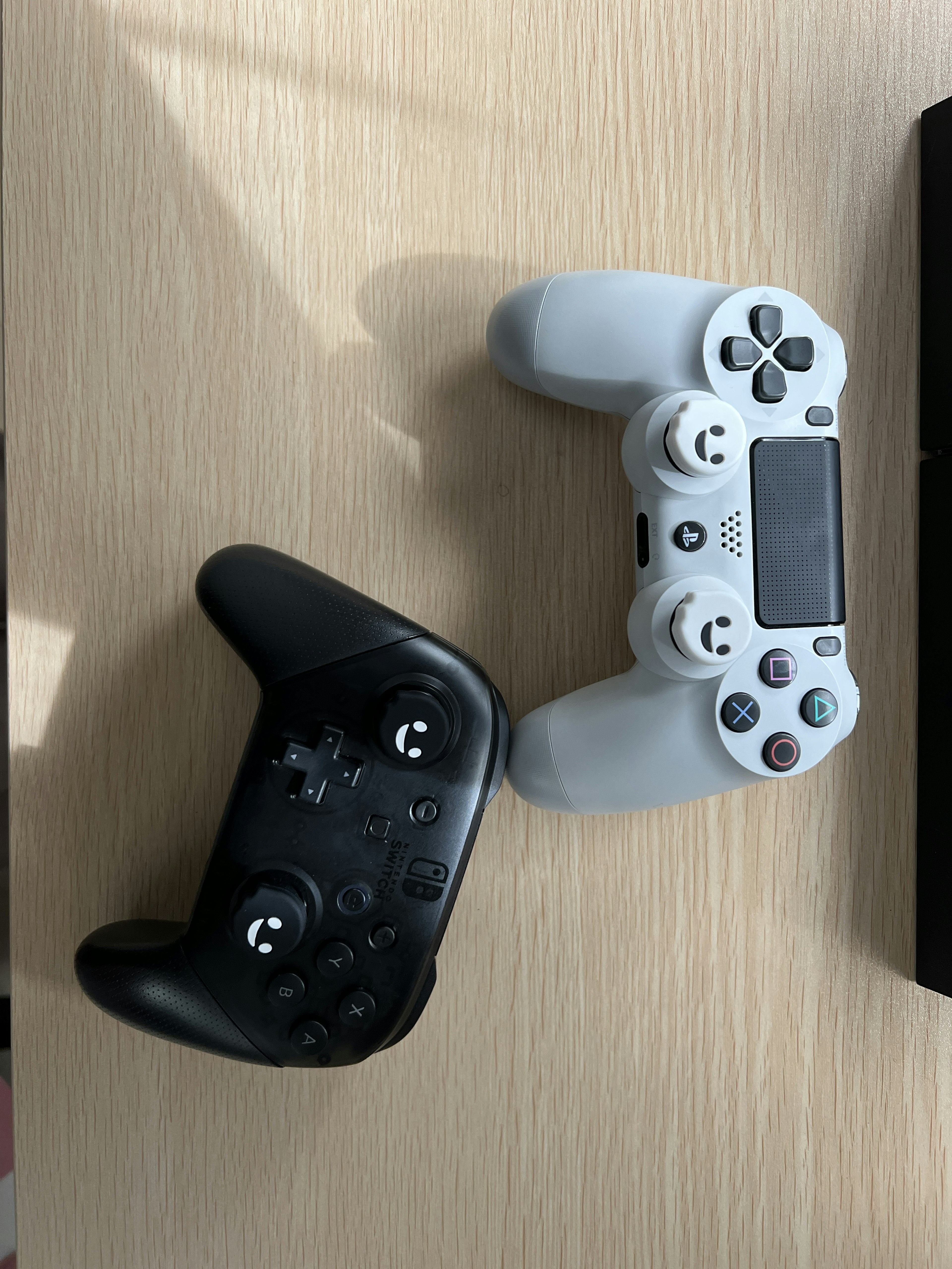 Black Xbox controller and white PlayStation controller placed on a wooden table