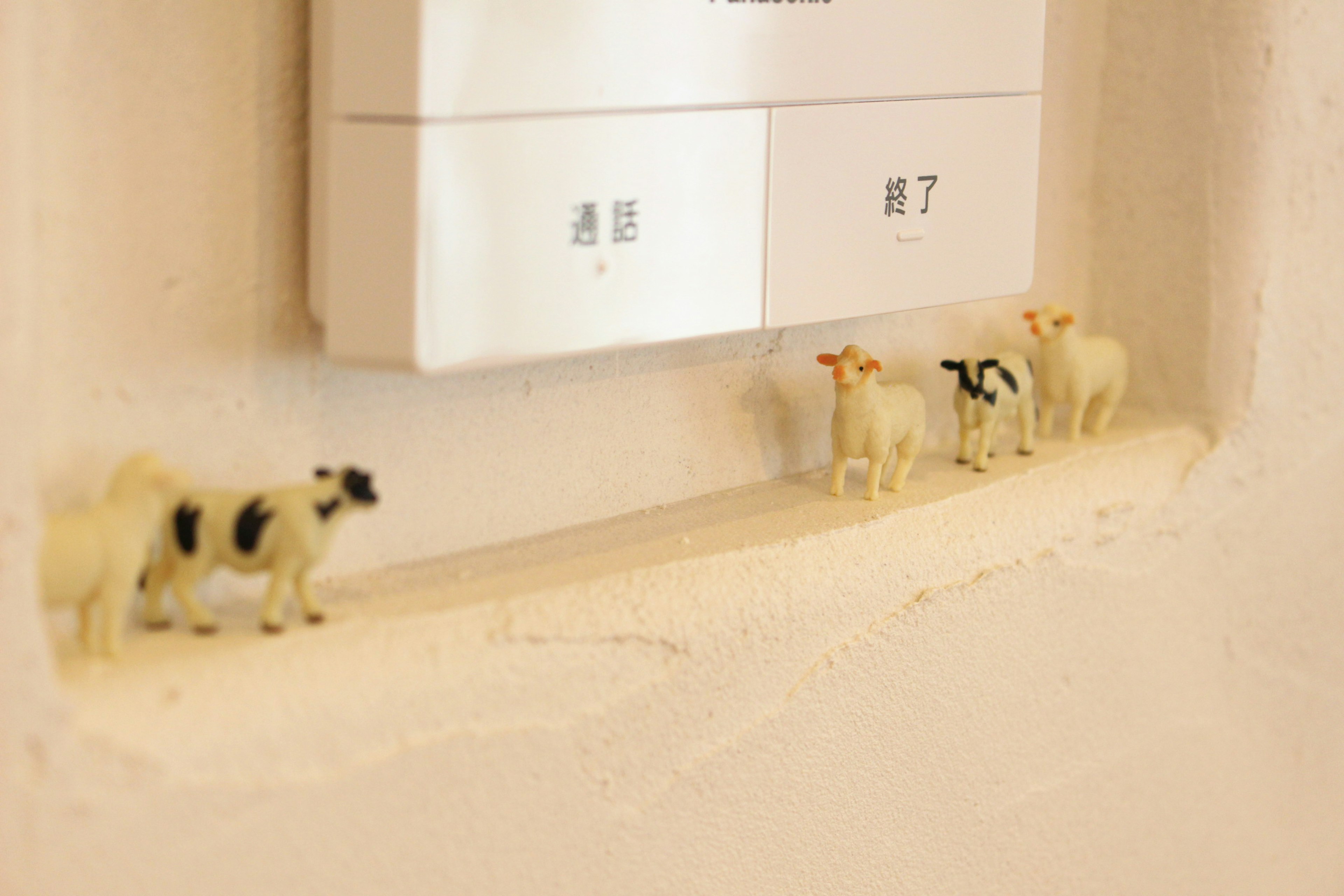 Small cow figurines lined up near a light switch on the wall