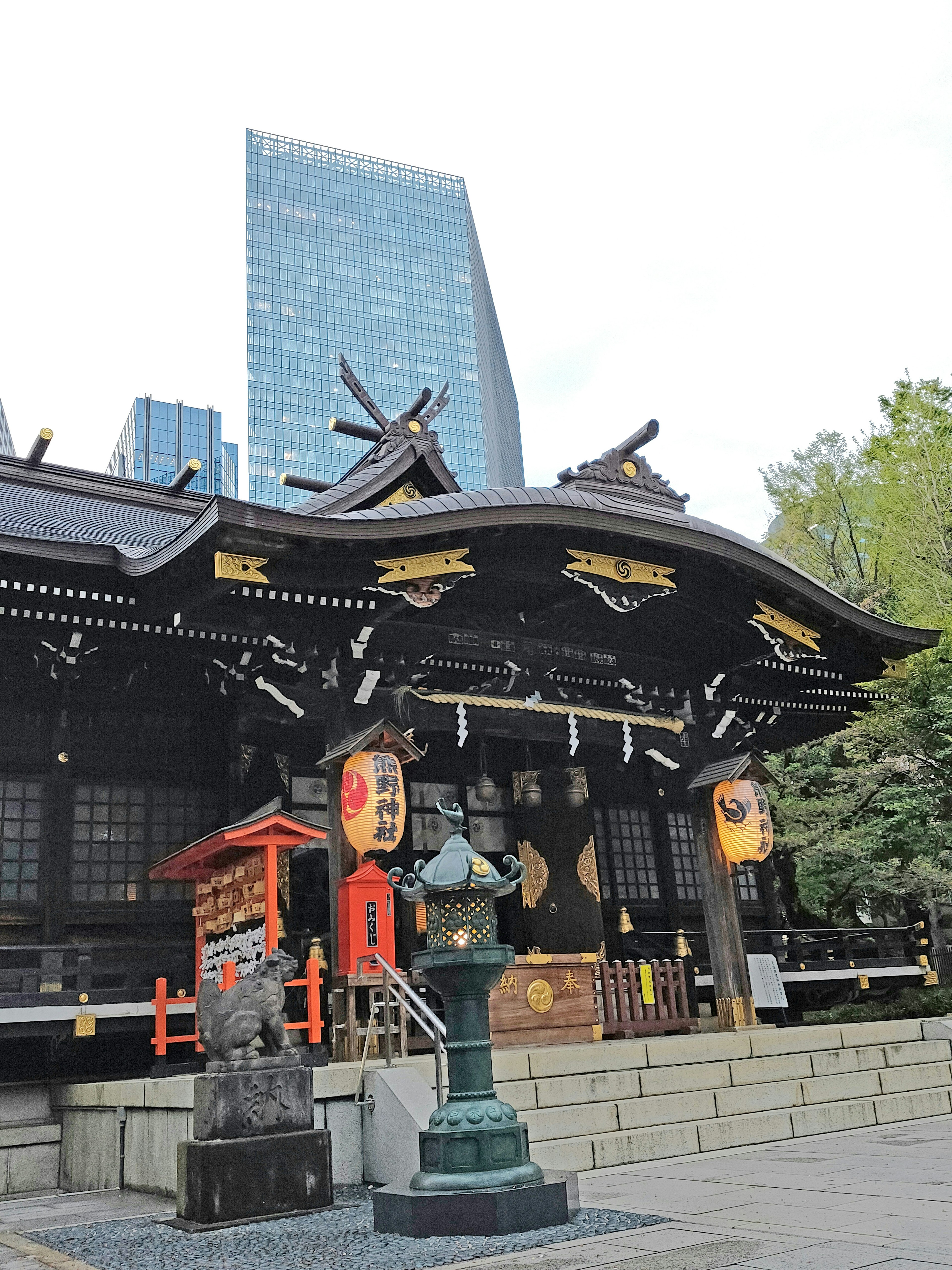 Traditional shrine building with lantern in foreground and modern skyscraper in background