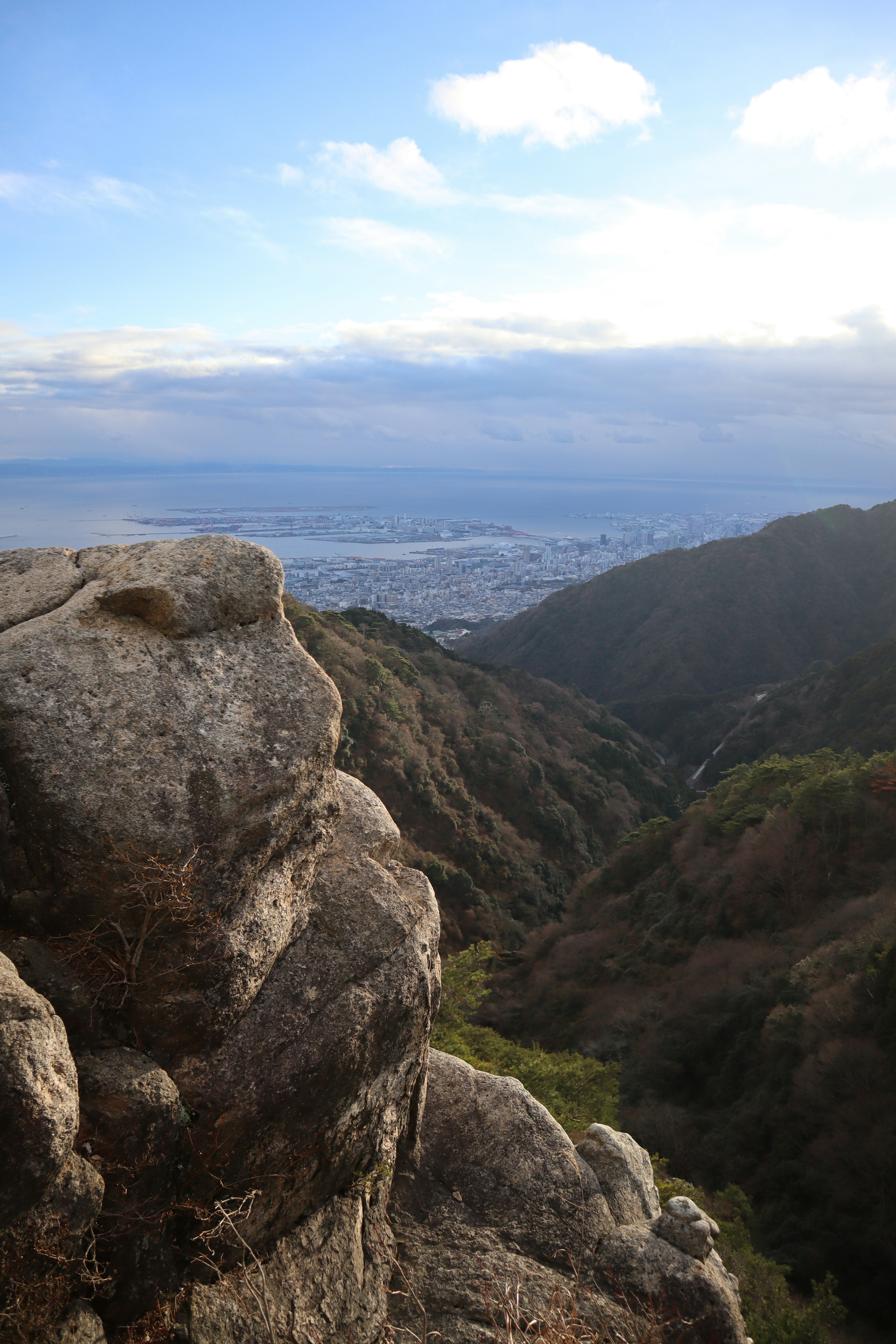 Vista desde la cima de una montaña mostrando un paisaje urbano distante con terreno rocoso y un valle