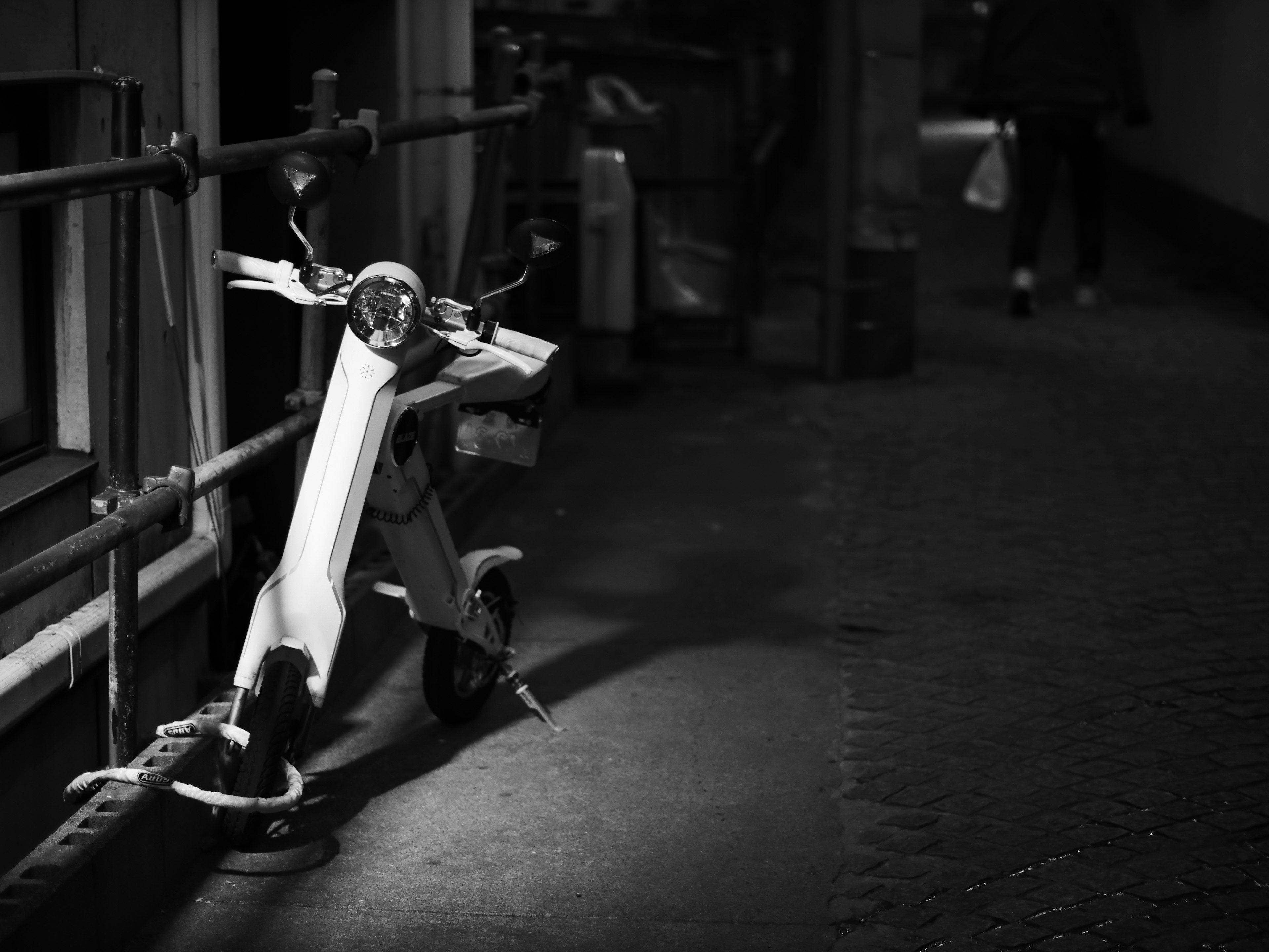 A black and white image of a scooter parked in a dimly lit alley