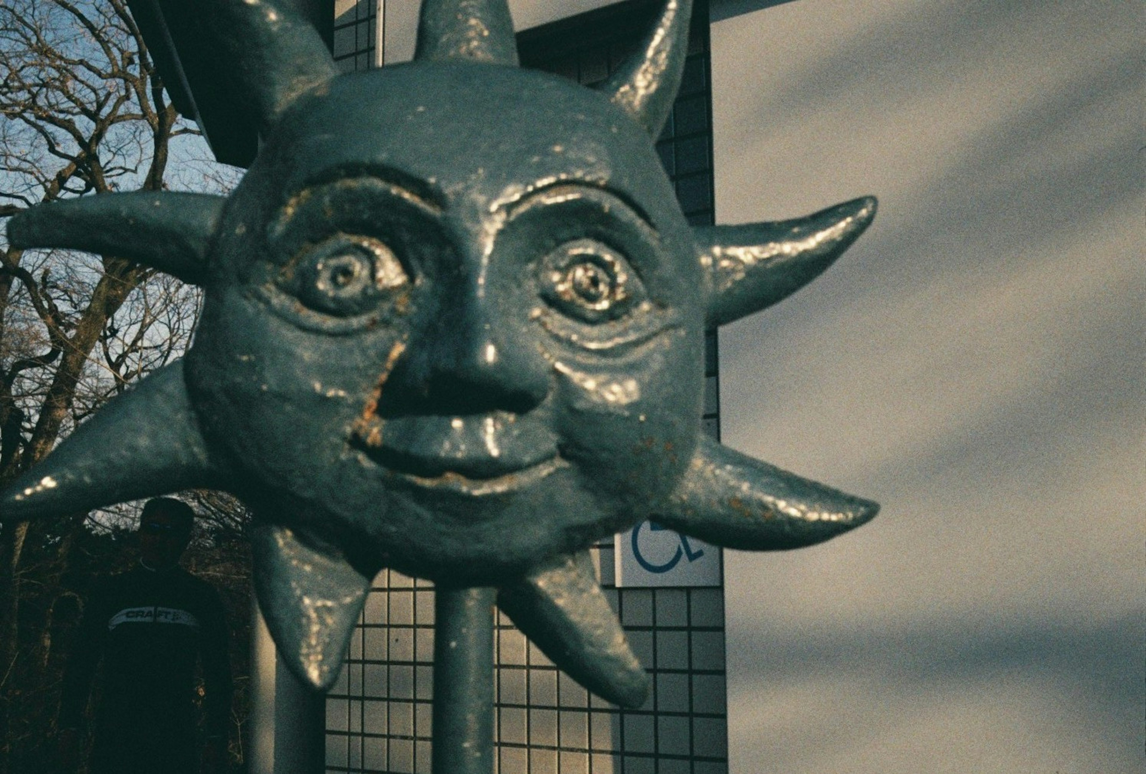 Escultura de metal de un rostro de sol con rayos y un fondo borroso