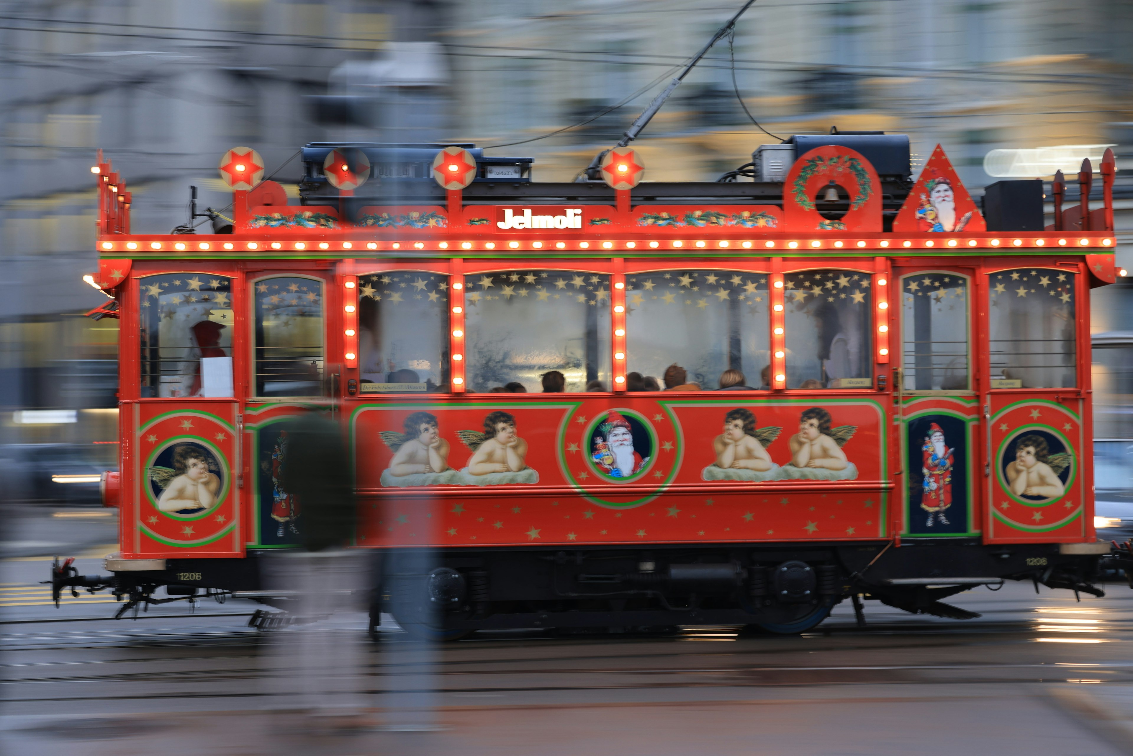 A vintage tram decorated in red with lights moving through the city