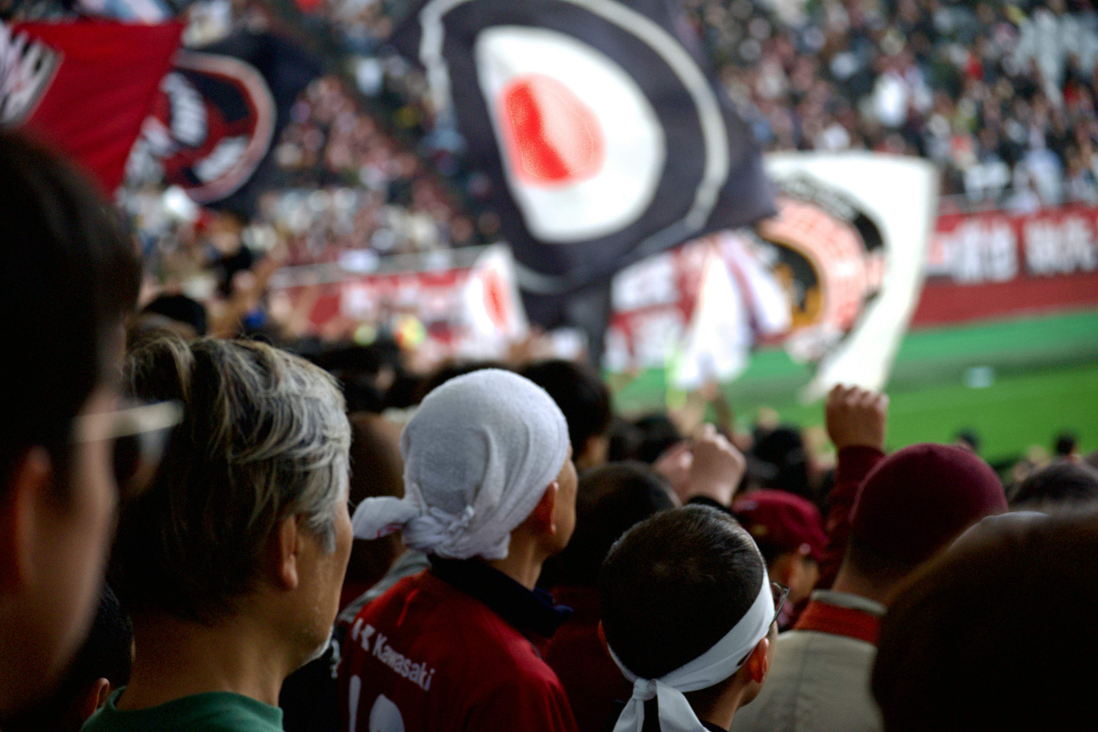 Folla di tifosi che tifano durante una partita di calcio con grandi bandiere