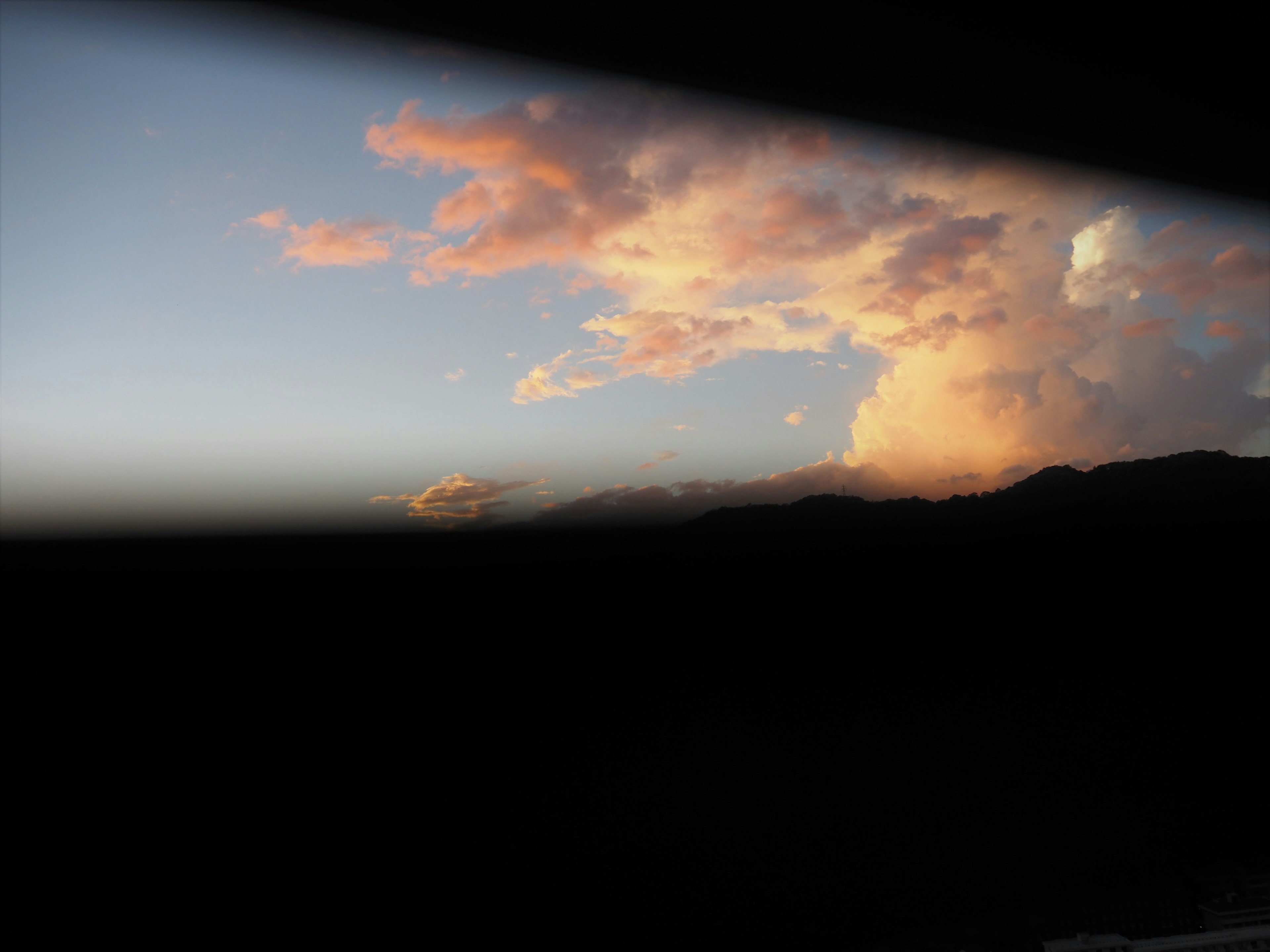 窓の隙間から見える夕焼けの空と雲