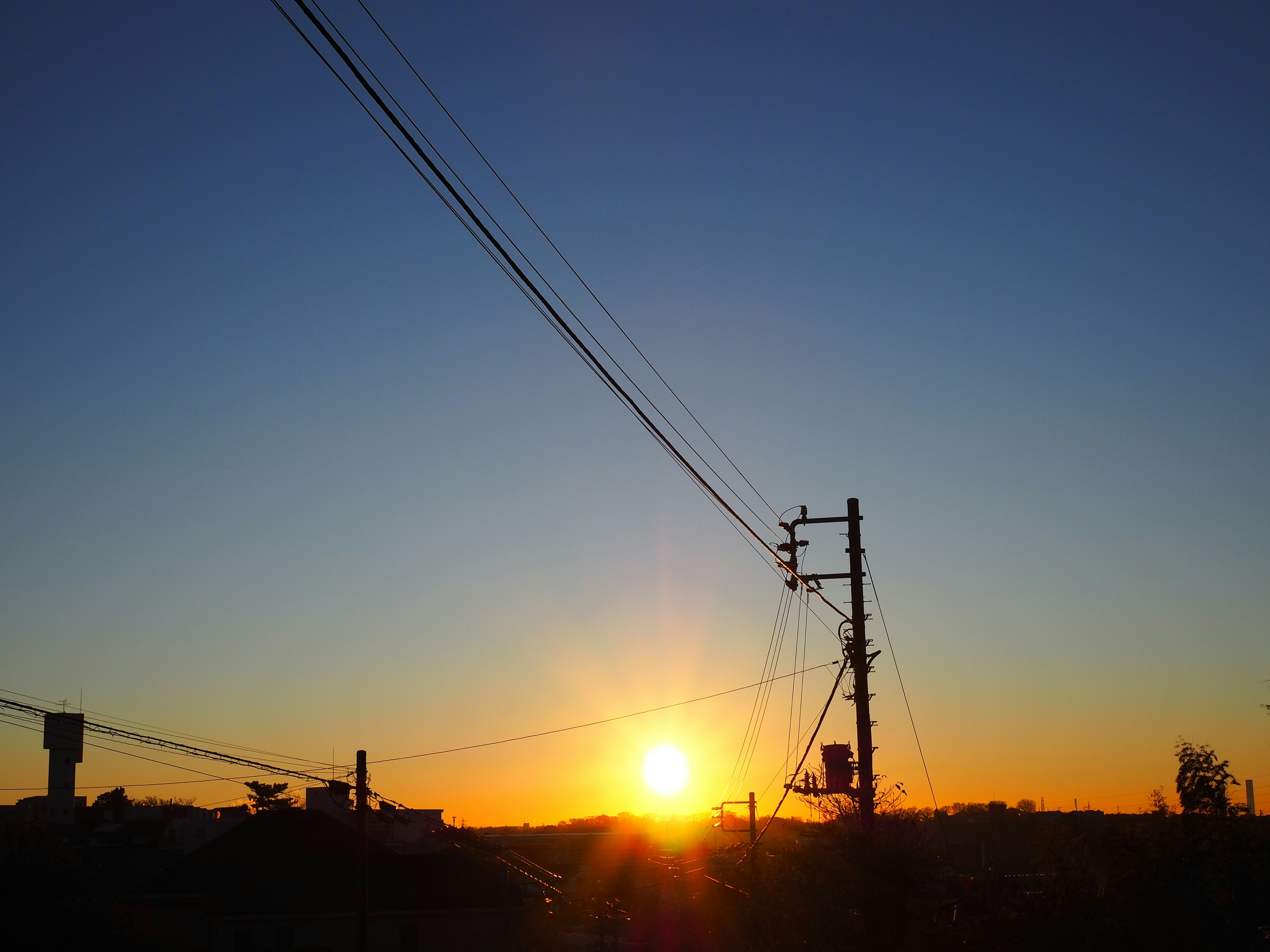 Sonnenuntergangslandschaft mit silhouettierten Gebäuden und Stromleitungen