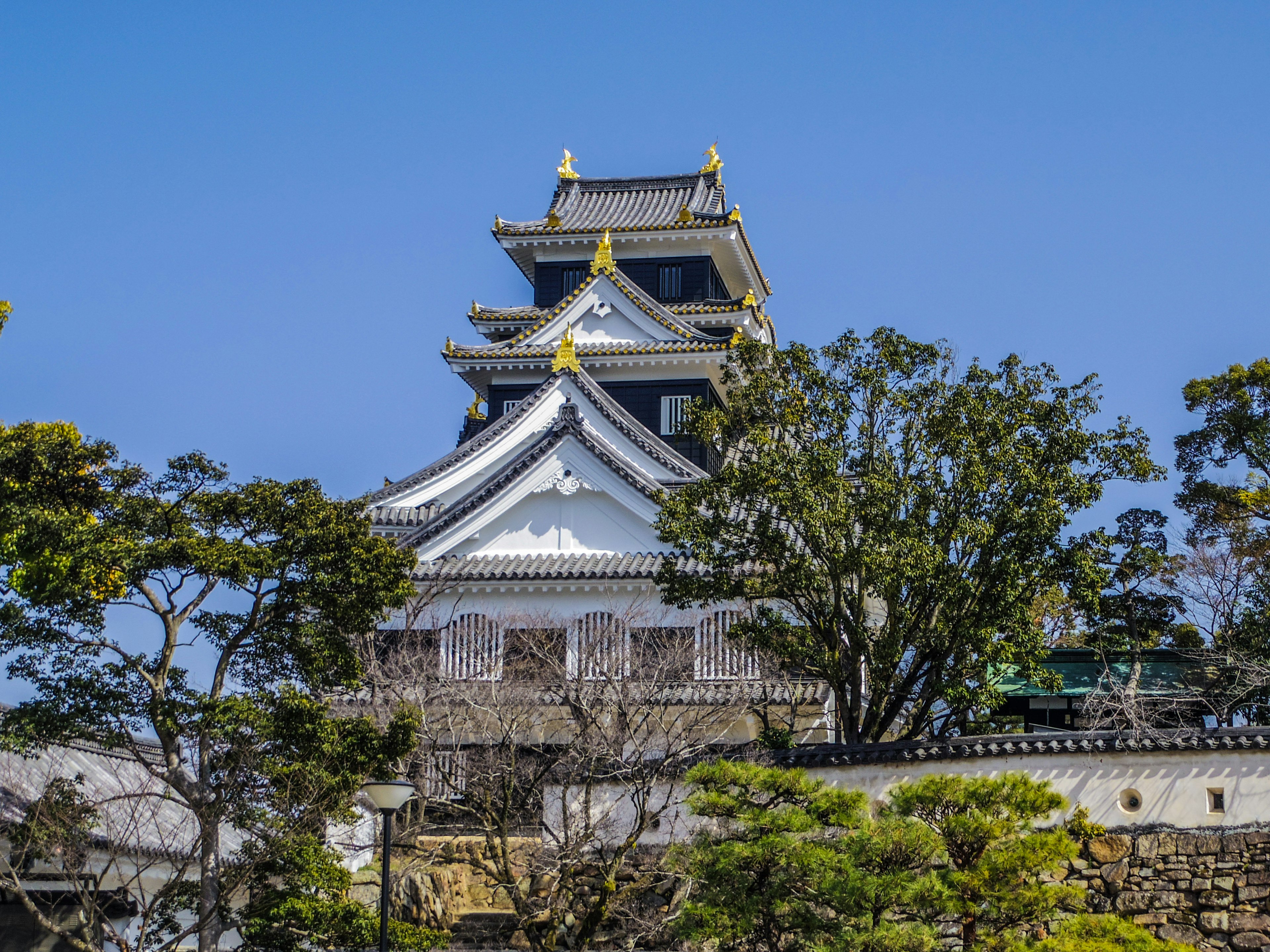 Castle tower with white walls and gold accents surrounded by green trees