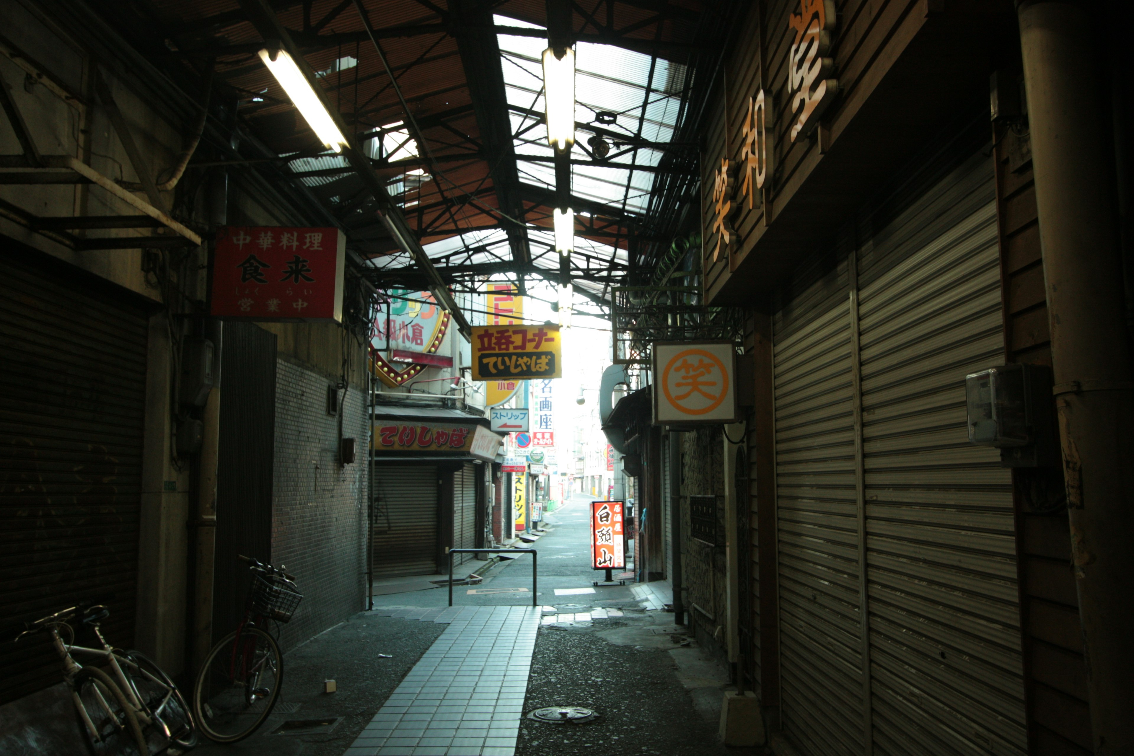 狭い路地にある閉店した店舗と自転車が見える