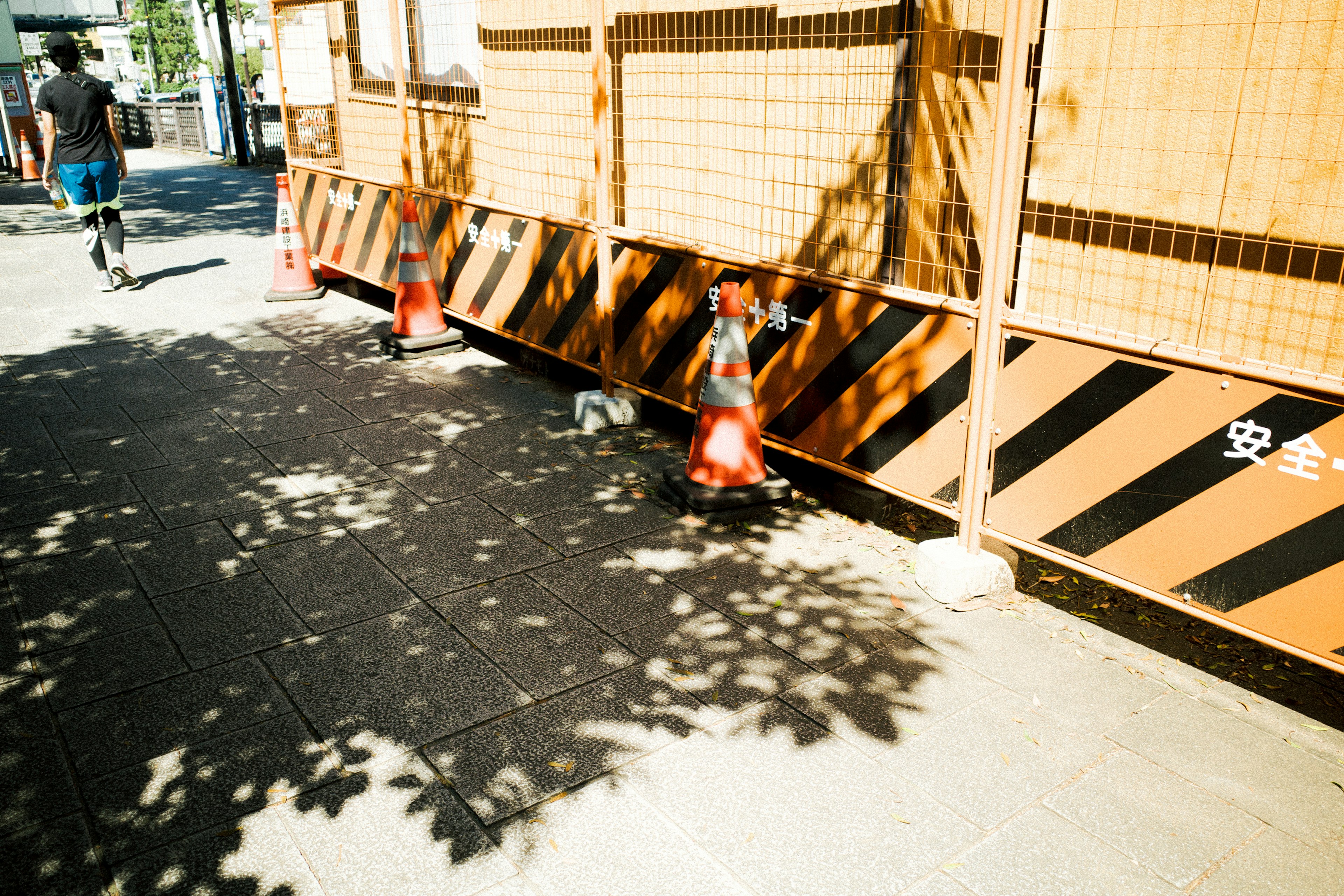 Conos de construcción en una acera con sombras y una barricada a rayas