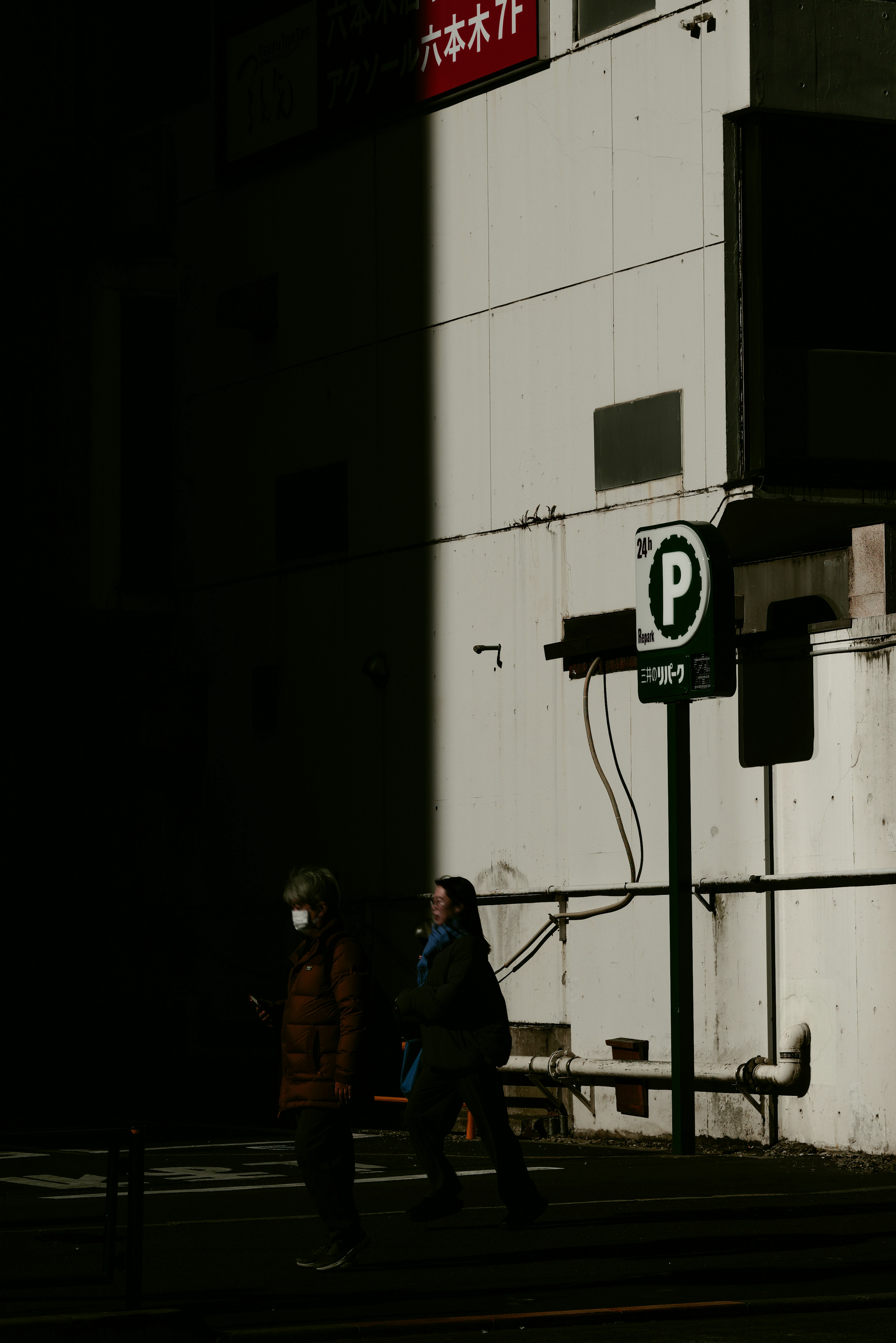 Zwei Personen, die im Schatten gehen, mit einem Parkplatzschild in einer städtischen Umgebung