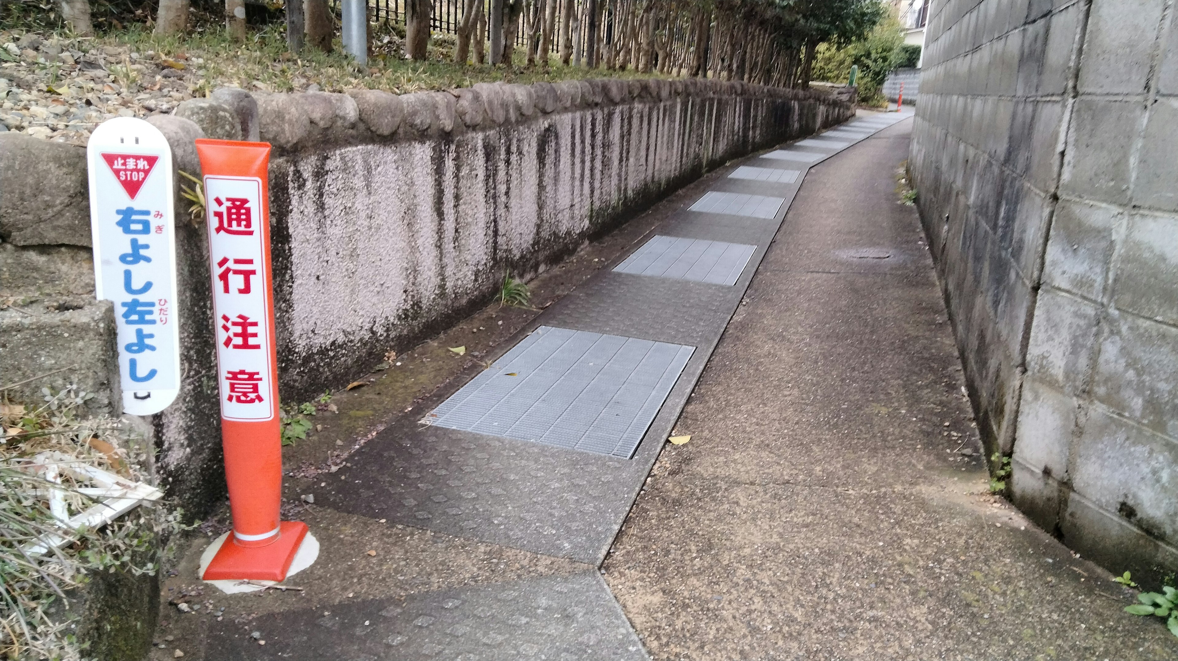 Narrow paved pathway with caution signs alongside