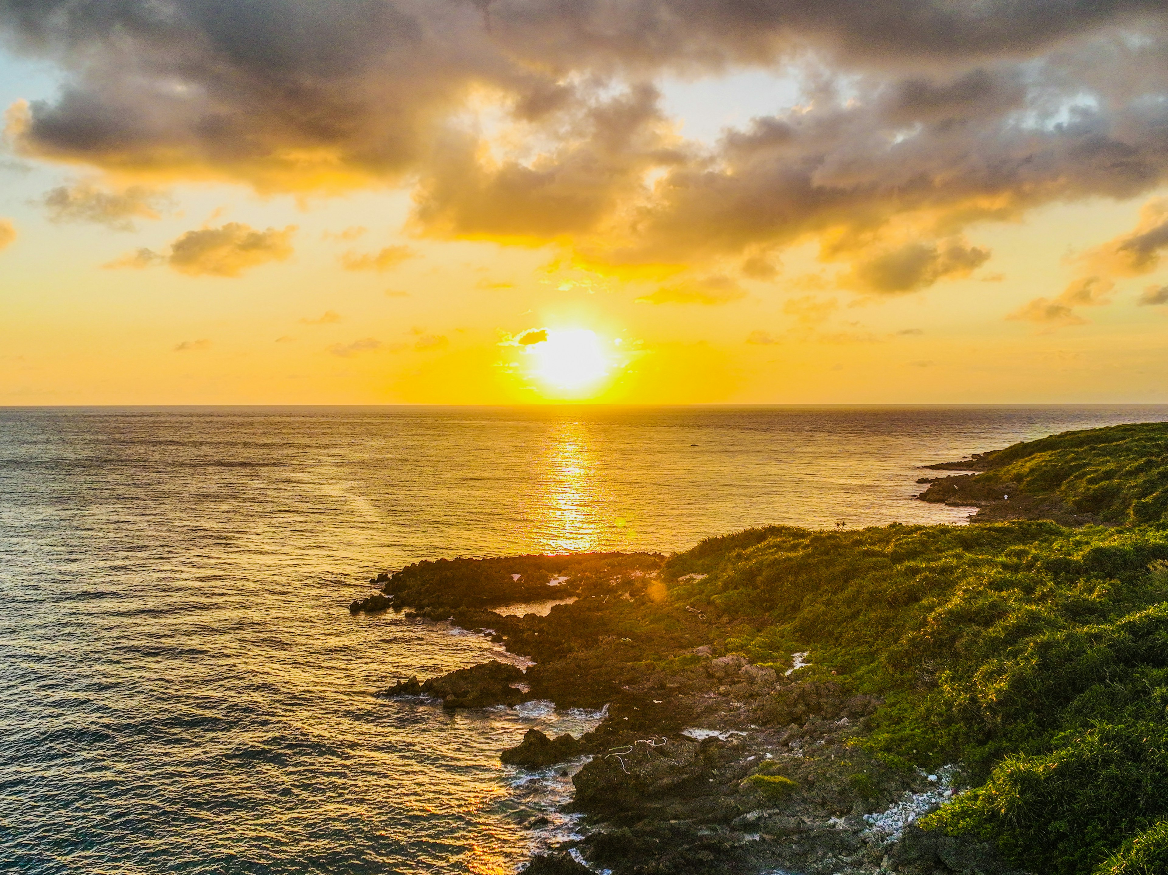 Wunderschöner Sonnenuntergang über dem Ozean mit üppiger Vegetation und felsiger Küste