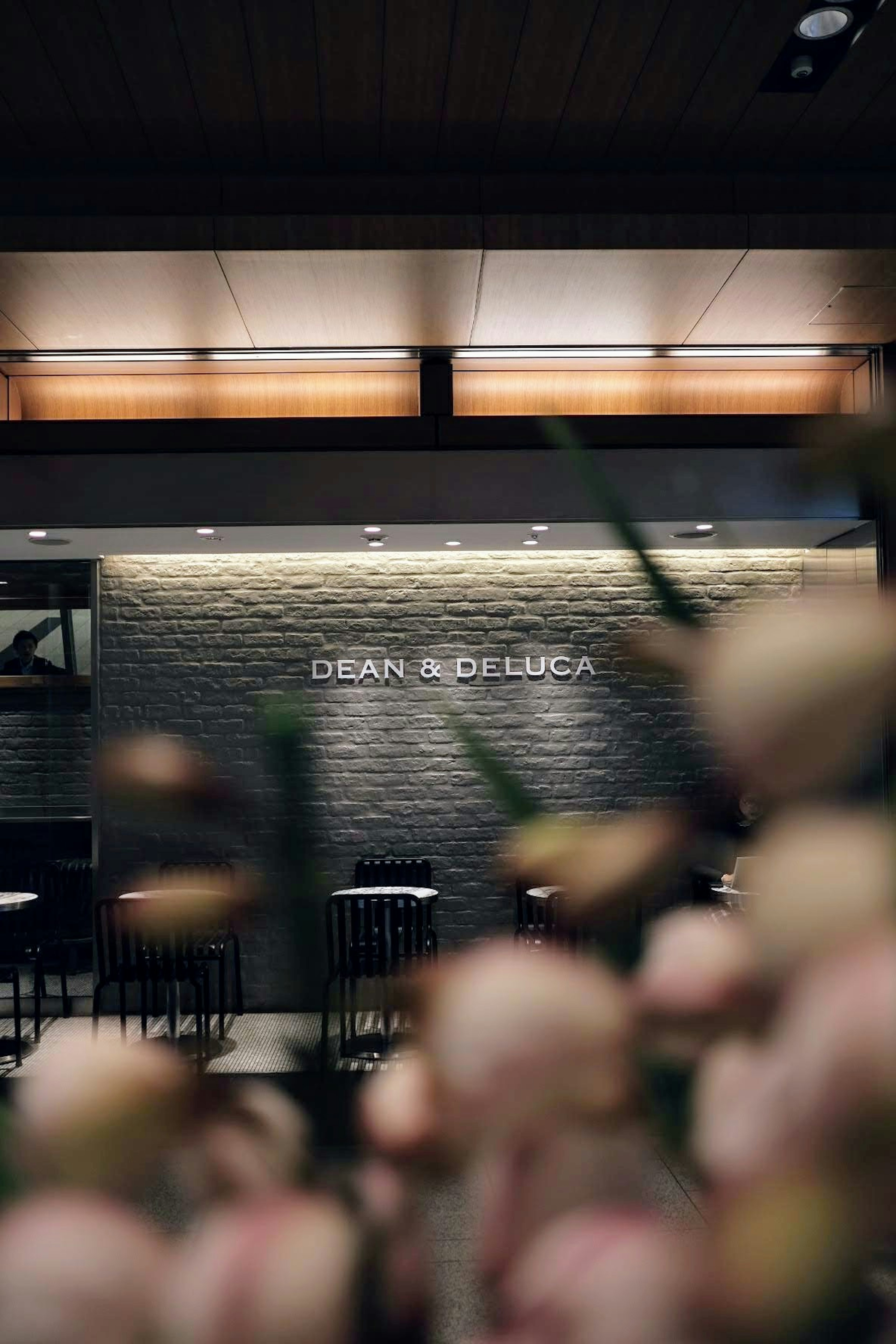 Interior view of a café with DEAN & DELUCA sign and flowers in the foreground