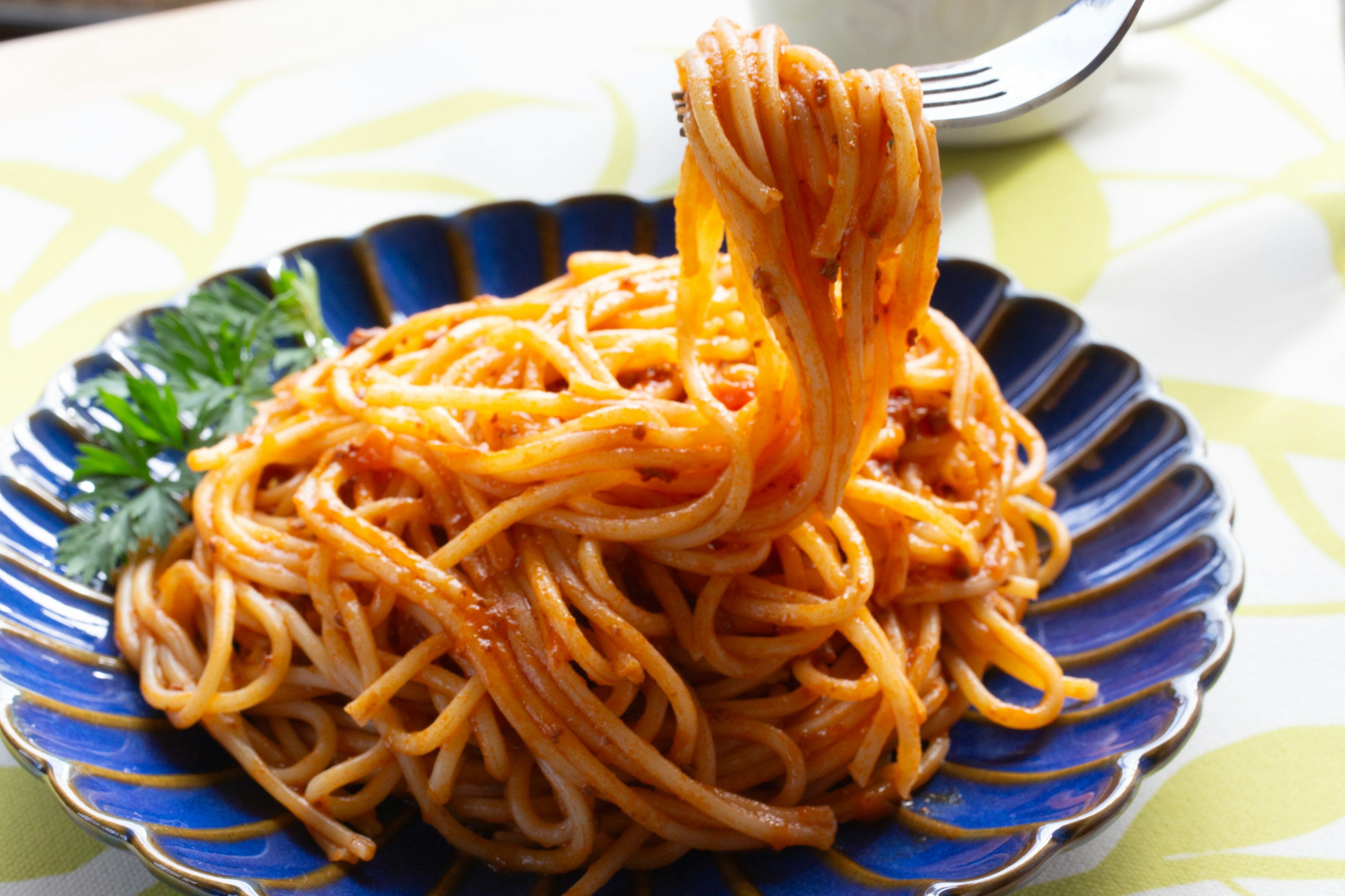 Spaghetti di atas piring biru dengan saus dan sebatang peterseli