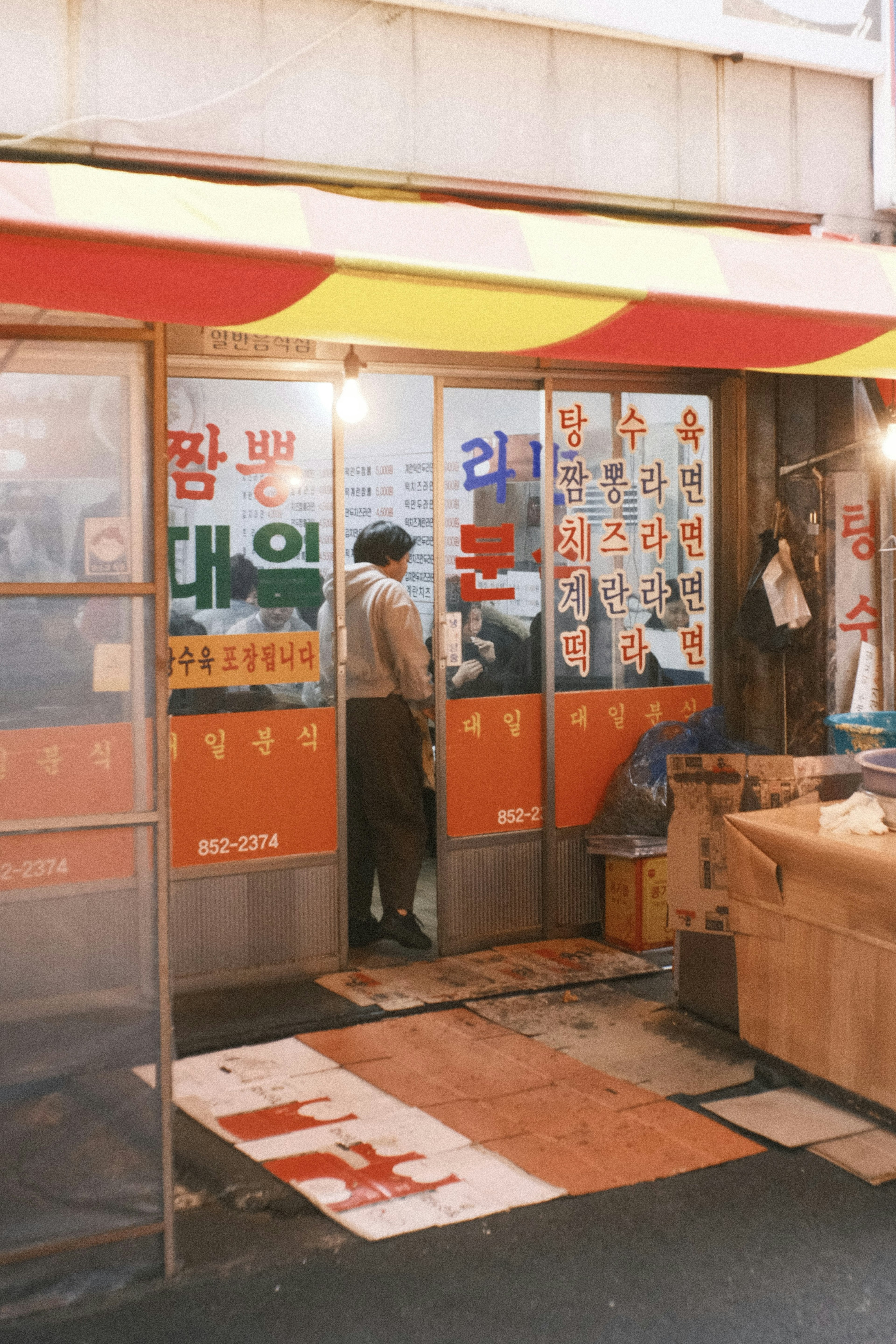 色とりどりの看板が並ぶ韓国の商店の外観 男性が扉の前に立っている