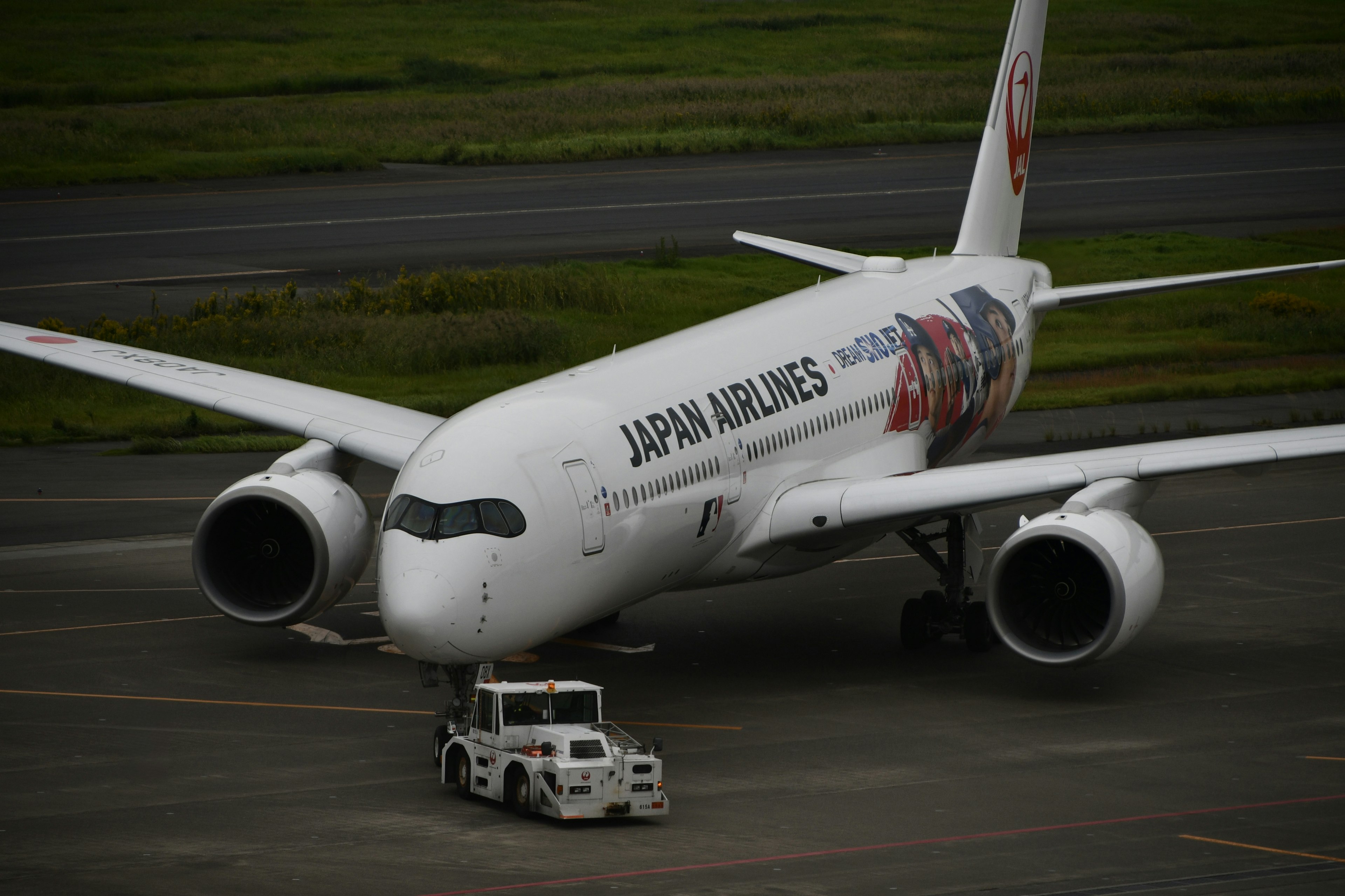 日本航空のボーイング787が滑走路でトーイングトラクターに牽引されている