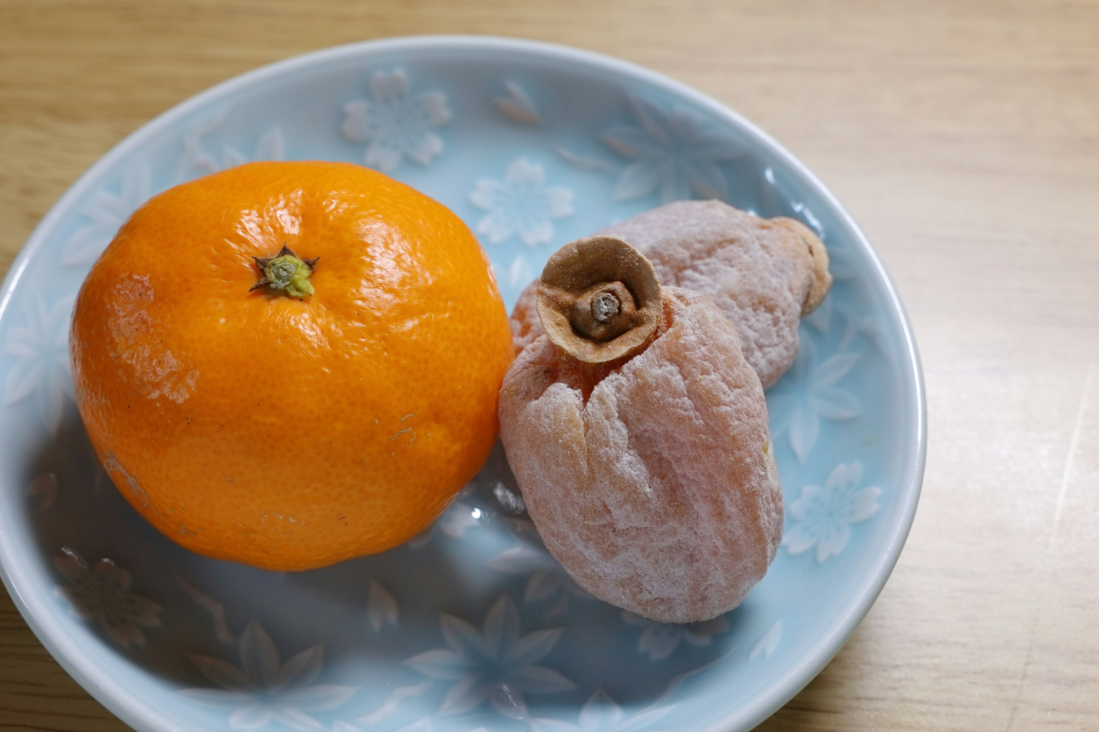 Sebuah mandarin oranye dan buah merah muda di atas piring biru