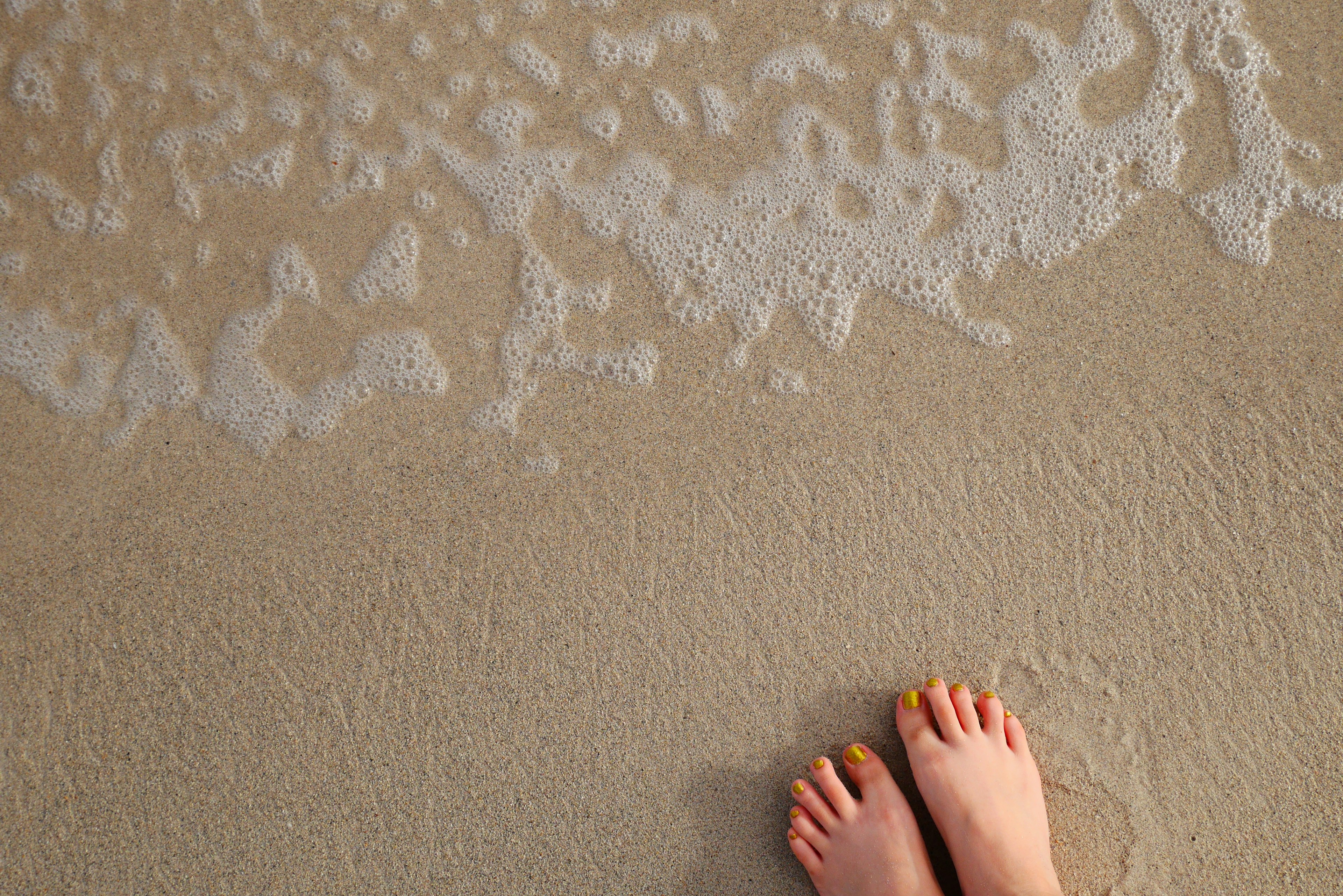 Bare feet standing on sandy beach with foamy waves