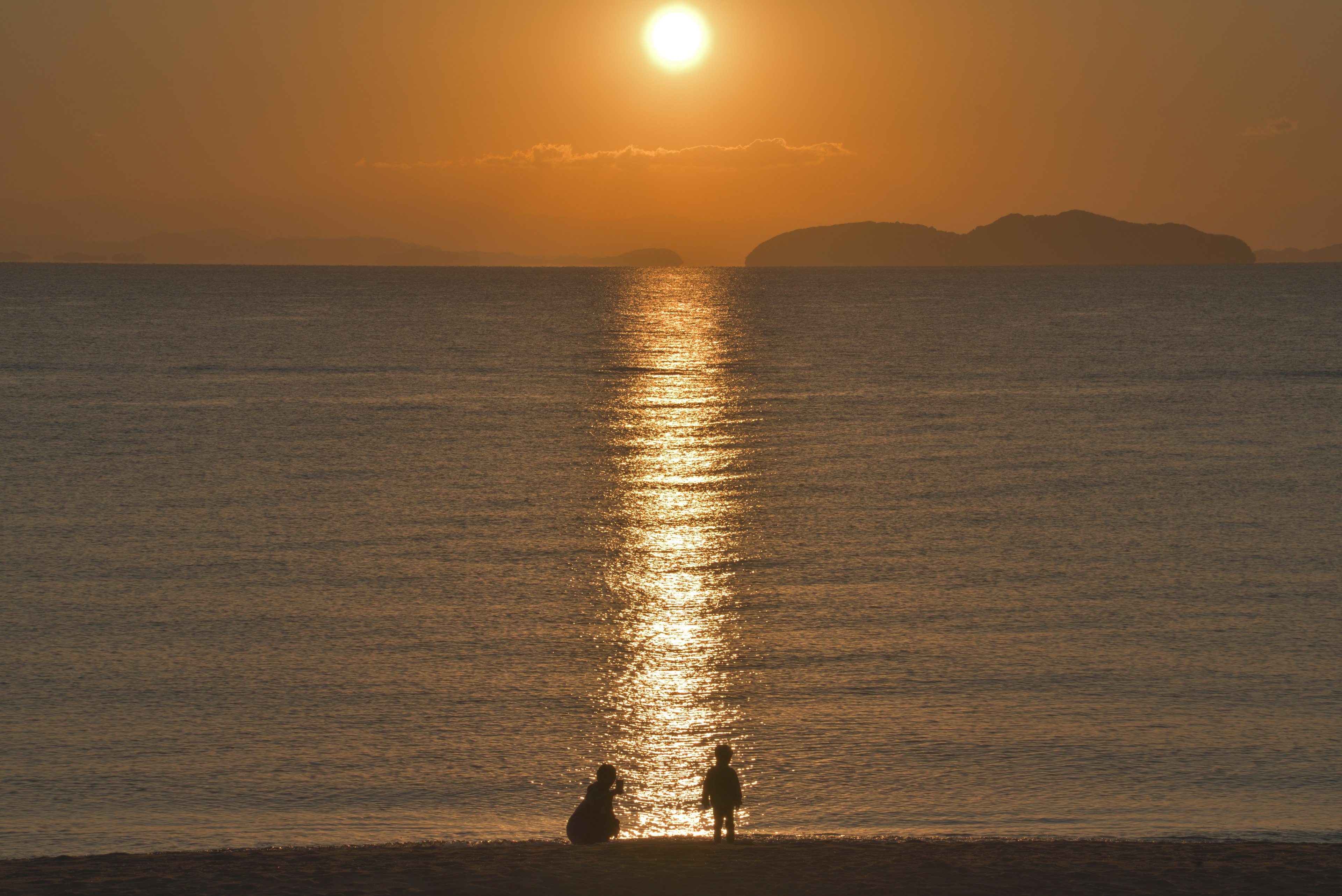 Silhouette of two people sitting on the beach with sunset reflecting on the ocean