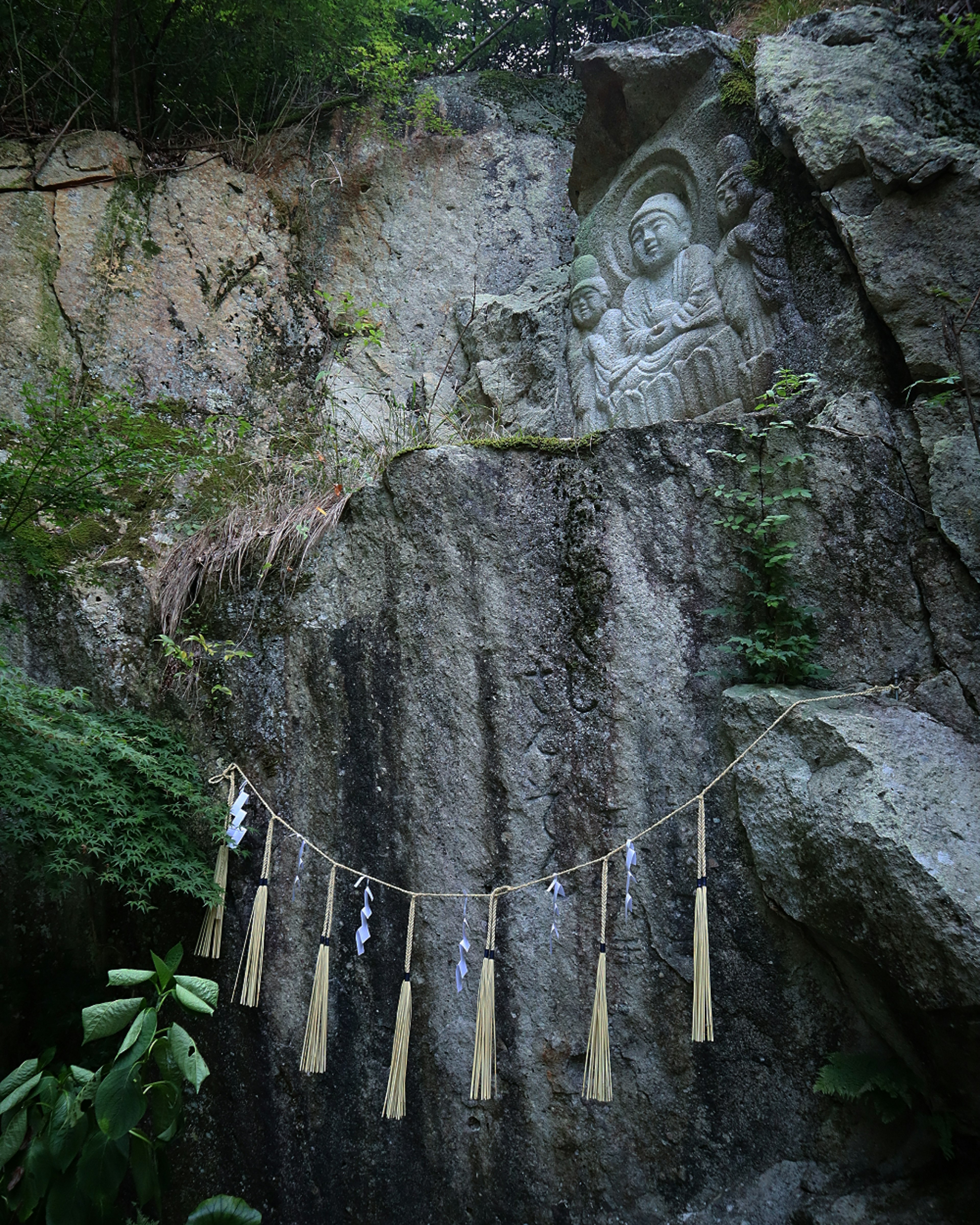 Rock carving of a Buddha and hanging bamboo decorations in a natural setting