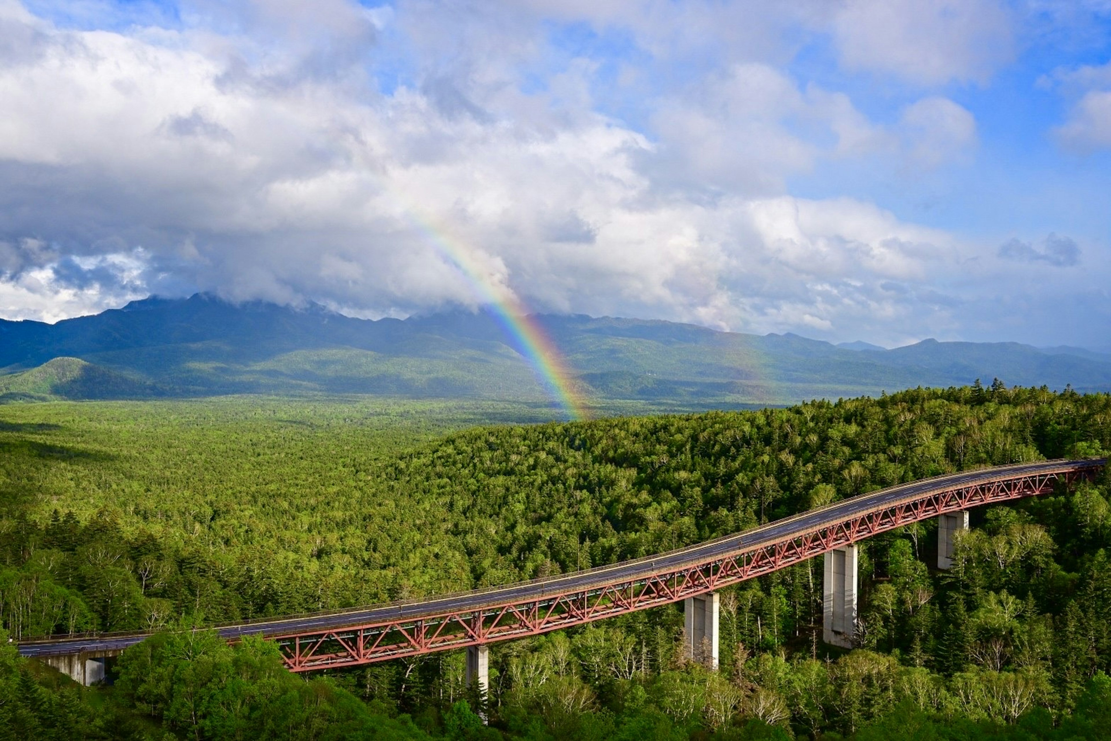 Un puente ferroviario con montañas verdes y un arcoíris en el cielo