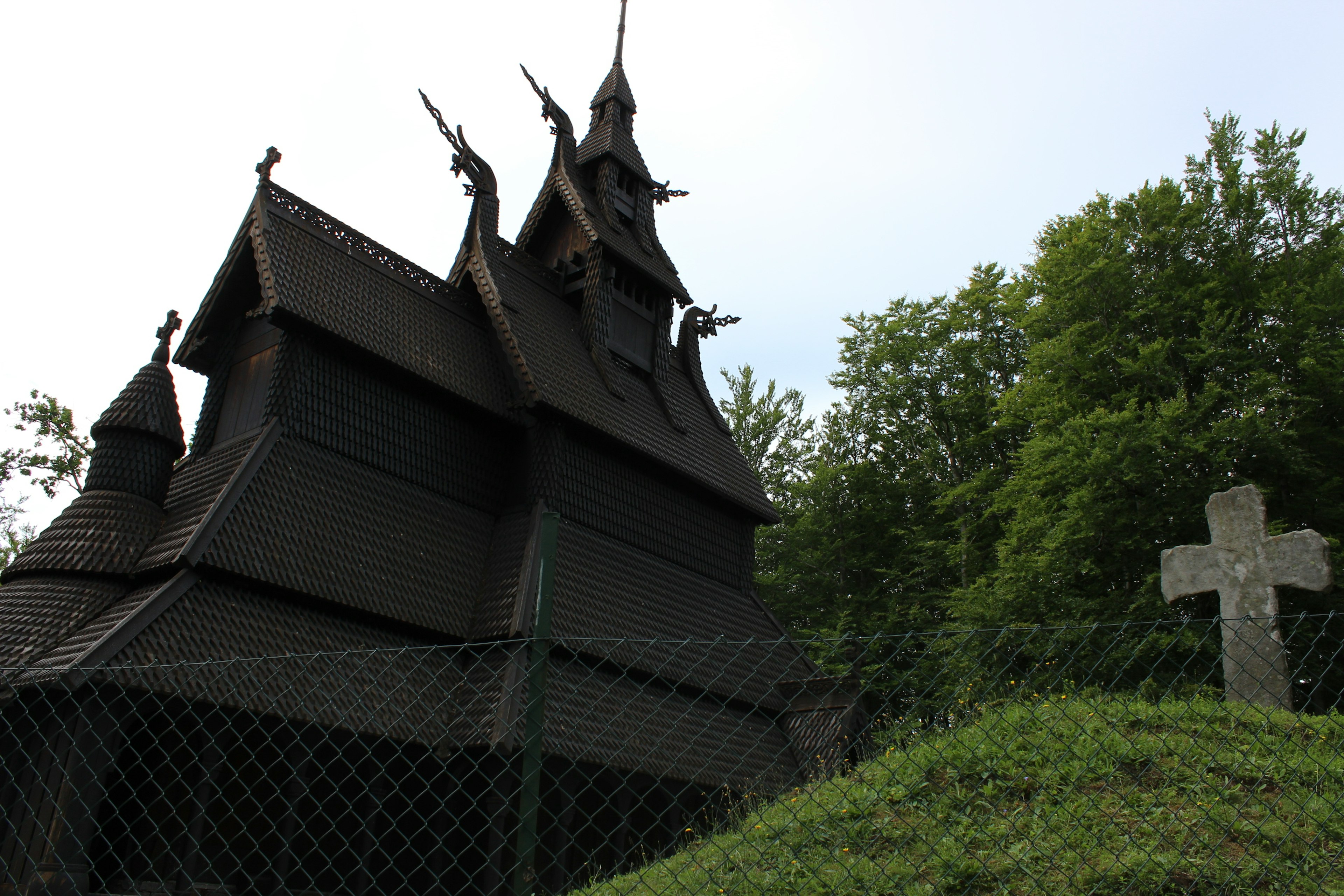 Extérieur d'une église en bois noir avec une croix en pierre à proximité