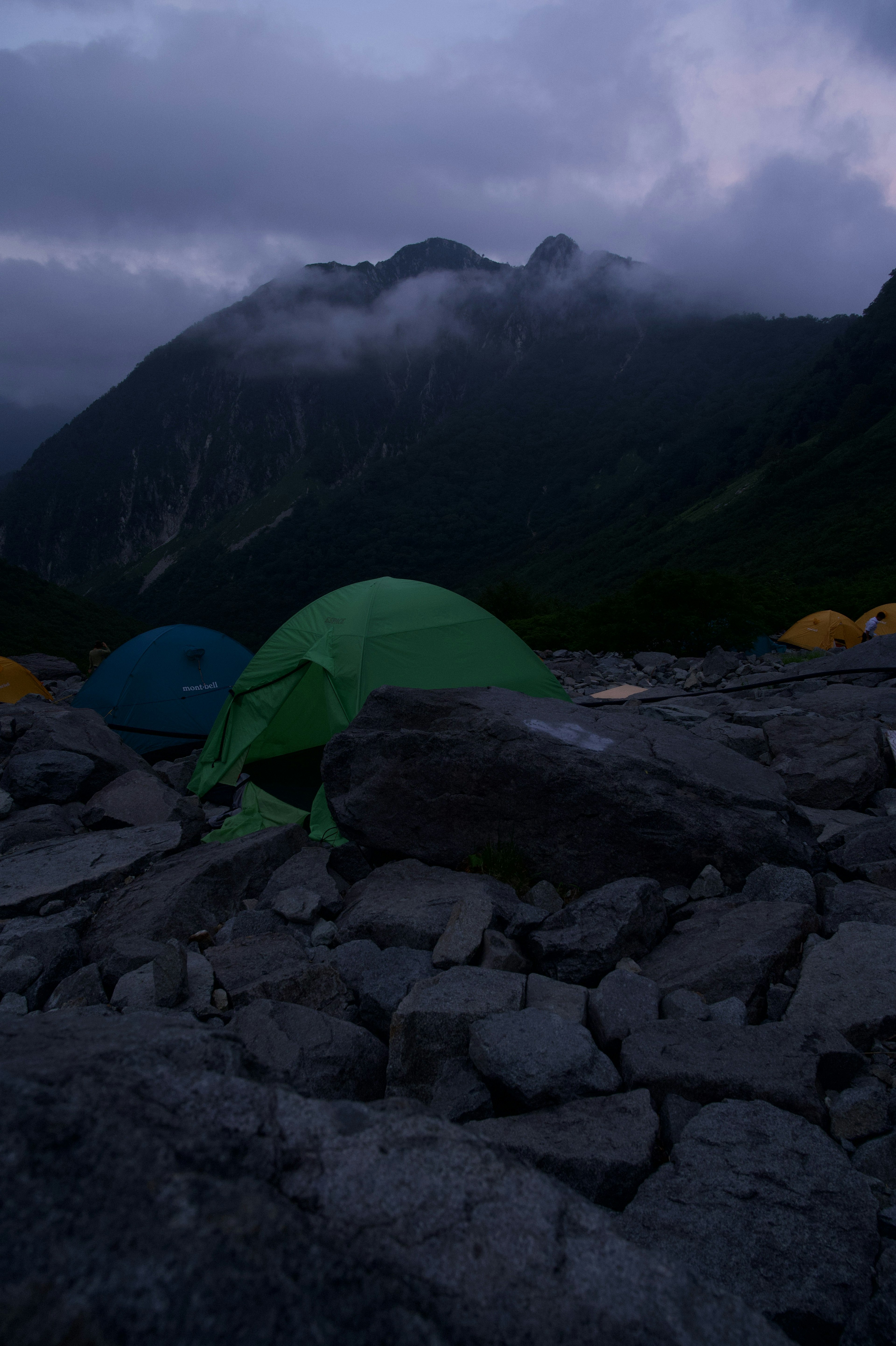 Blaue und grüne Zelte auf felsigem Gelände unter einer dunklen Berglandschaft