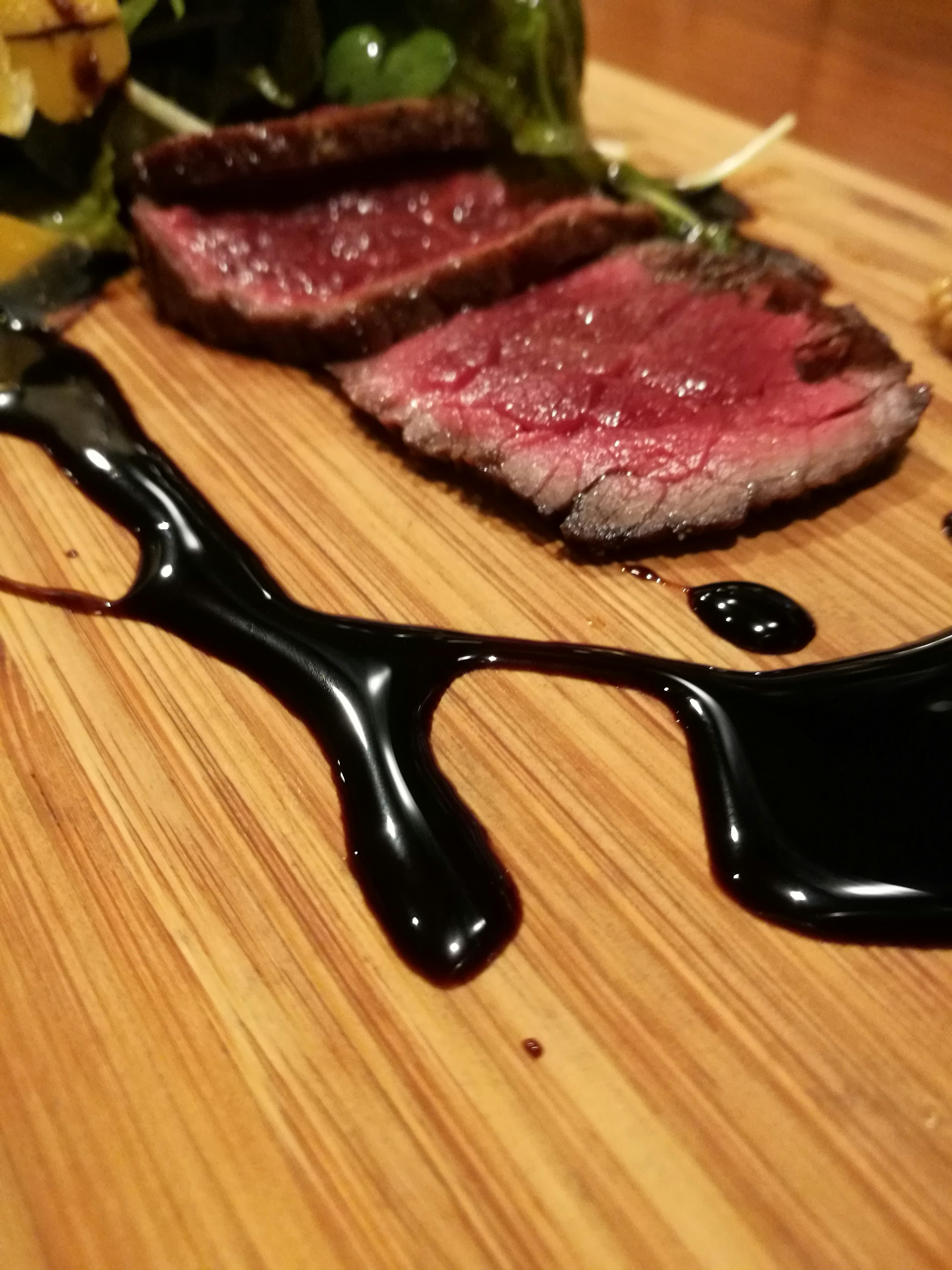 Sliced steak on a wooden board with dark sauce