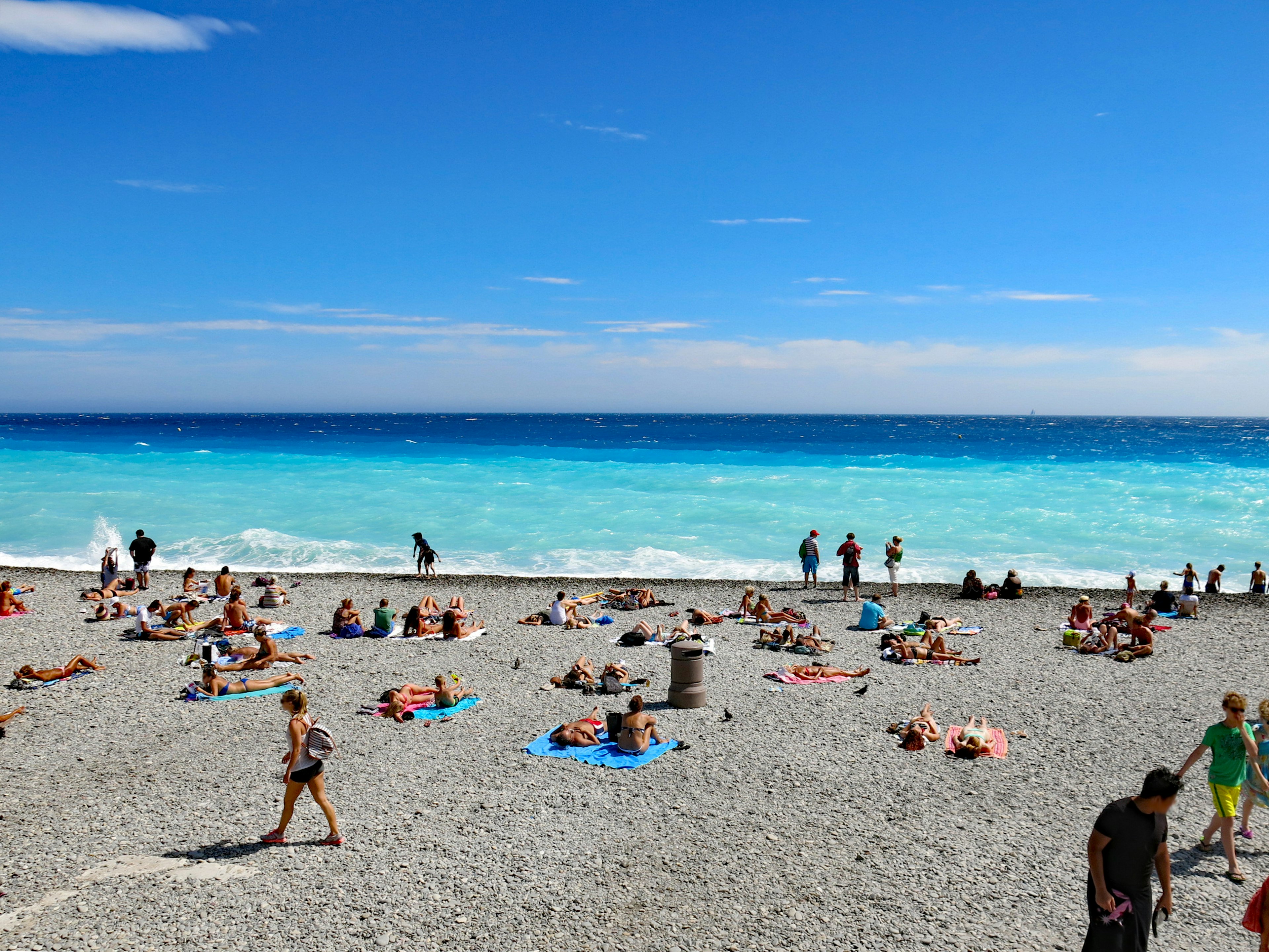 Strandszene mit Menschen, die sich auf Kieseln entspannen und einem lebhaften blauen Ozean