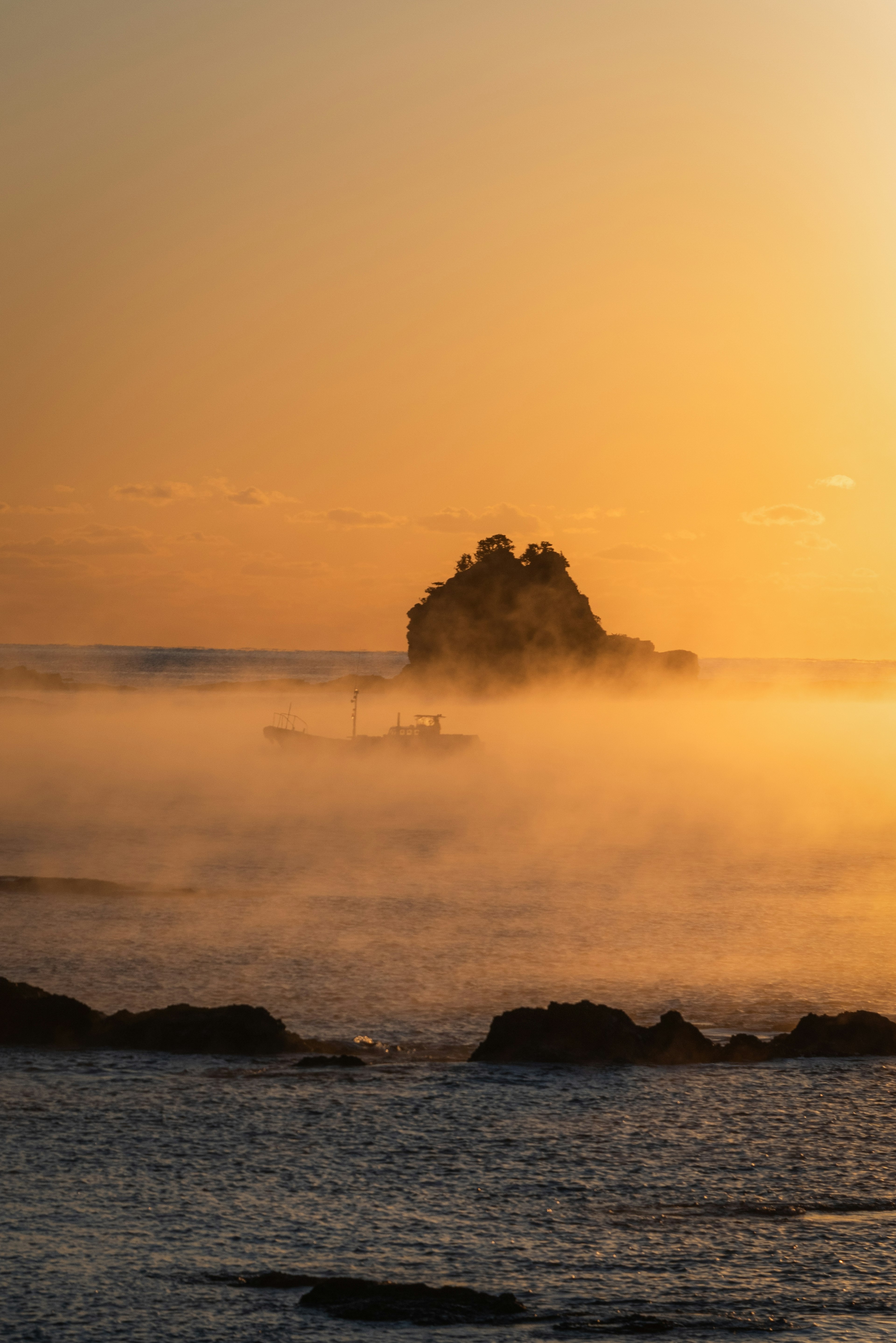 Isolierter Felsen in Nebel gehüllt mit Sonnenuntergangshorizont über dem Ozean