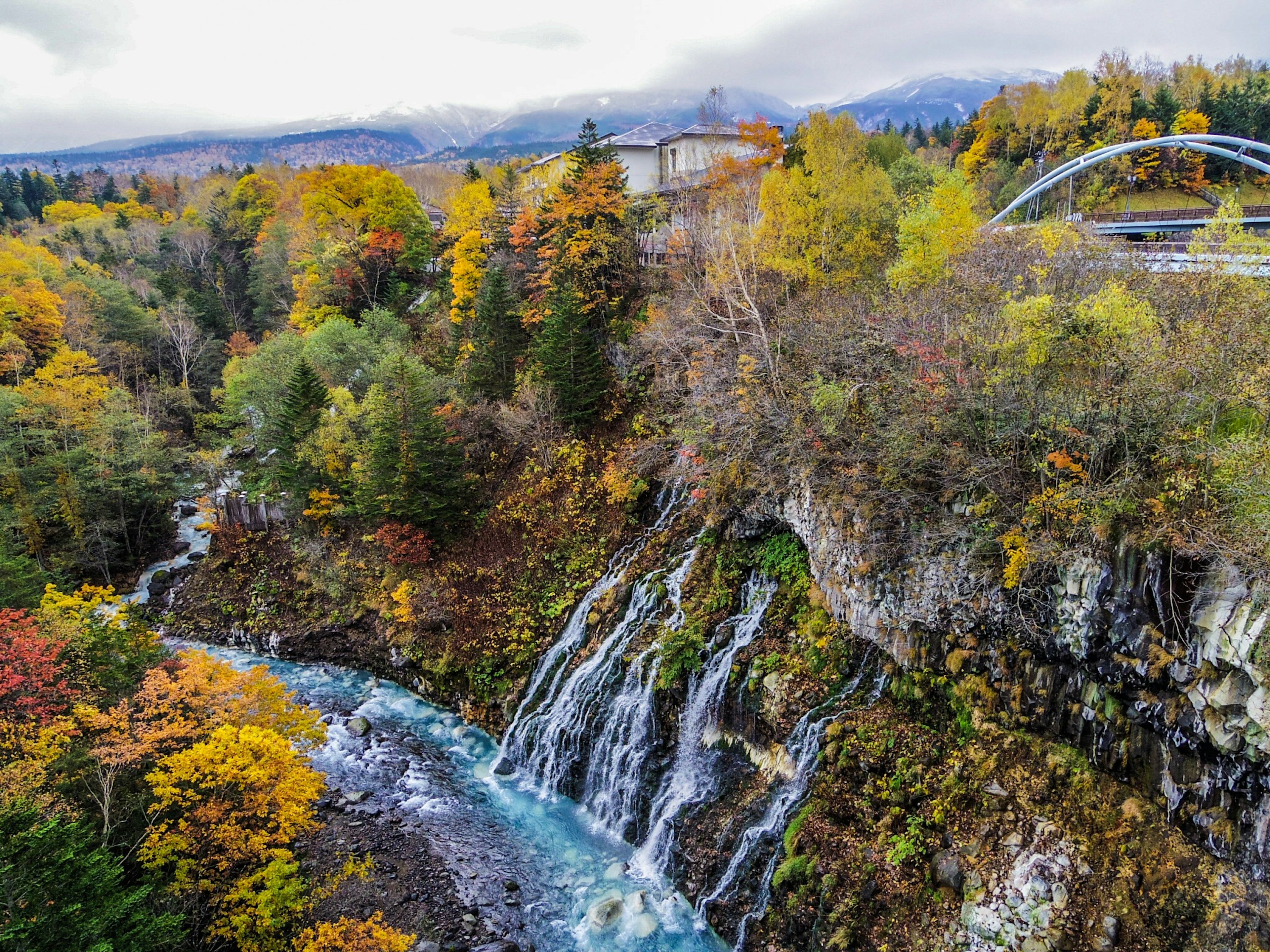 Vista escénica de una cascada y un río rodeados de follaje otoñal con árboles verdes y naranjas vibrantes