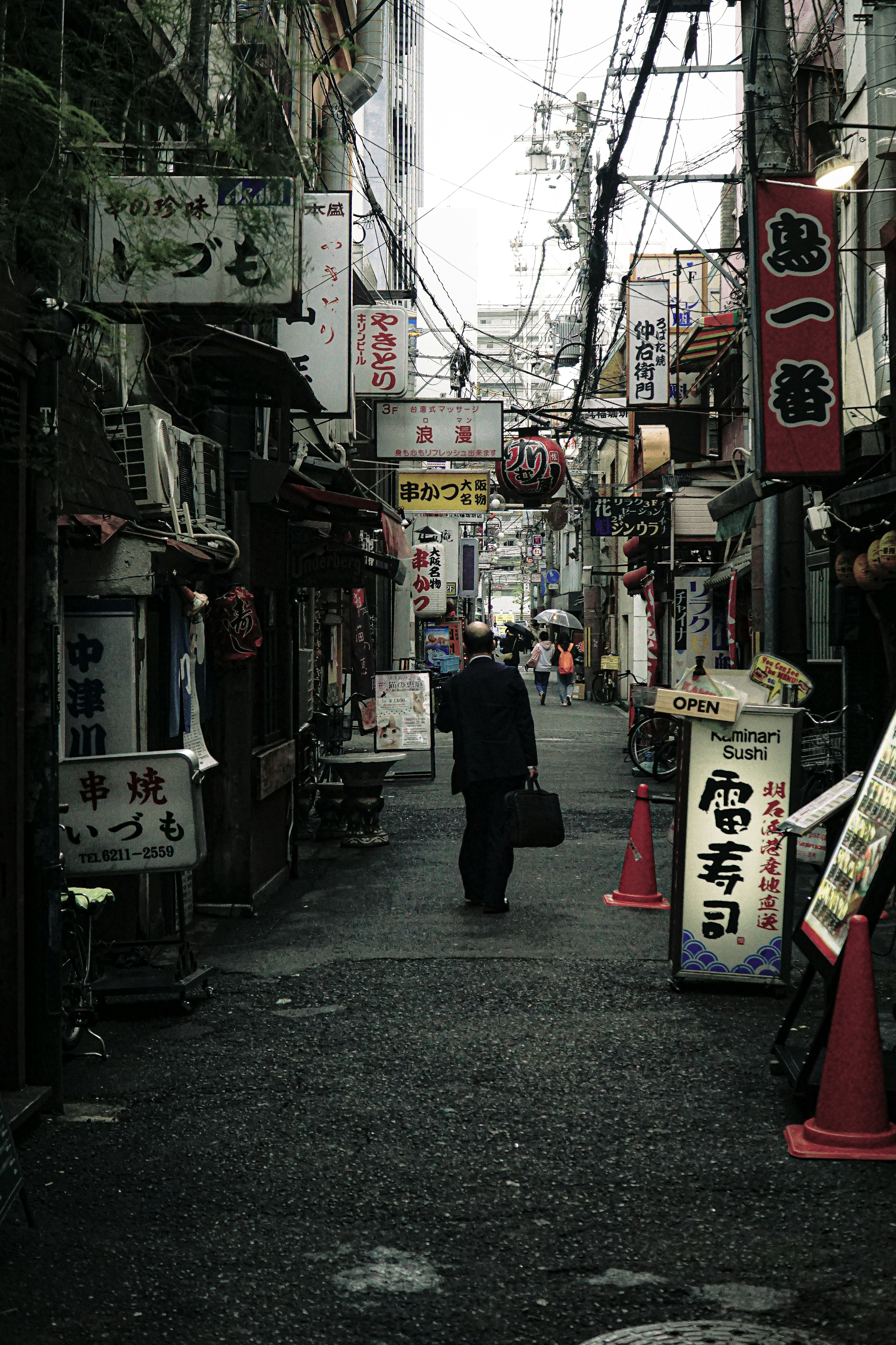 A suited man walking through a narrow alley with various signs and storefronts