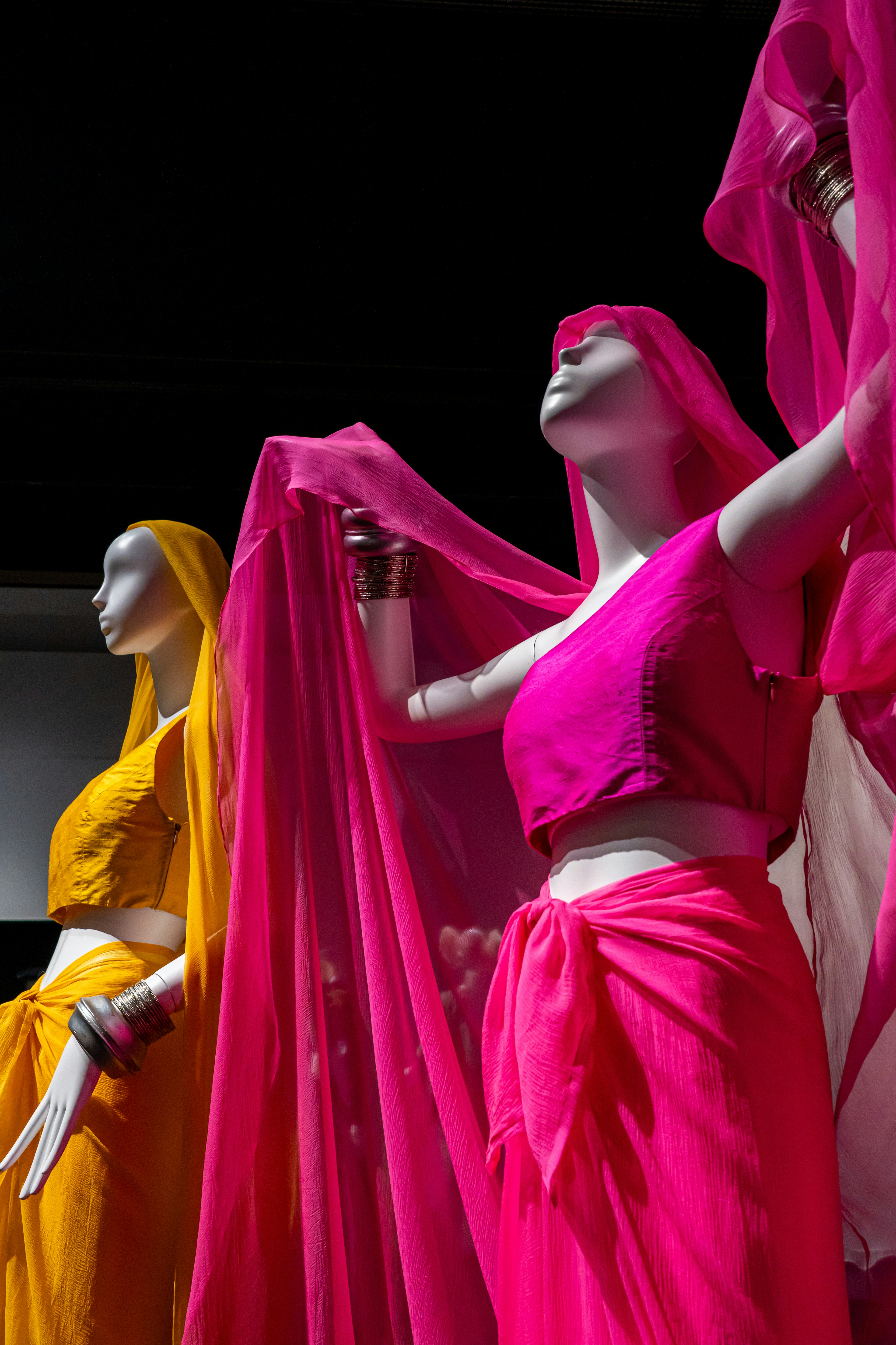 Manichini vestiti con sari vibranti rosa e giallo che mostrano abbigliamento tradizionale