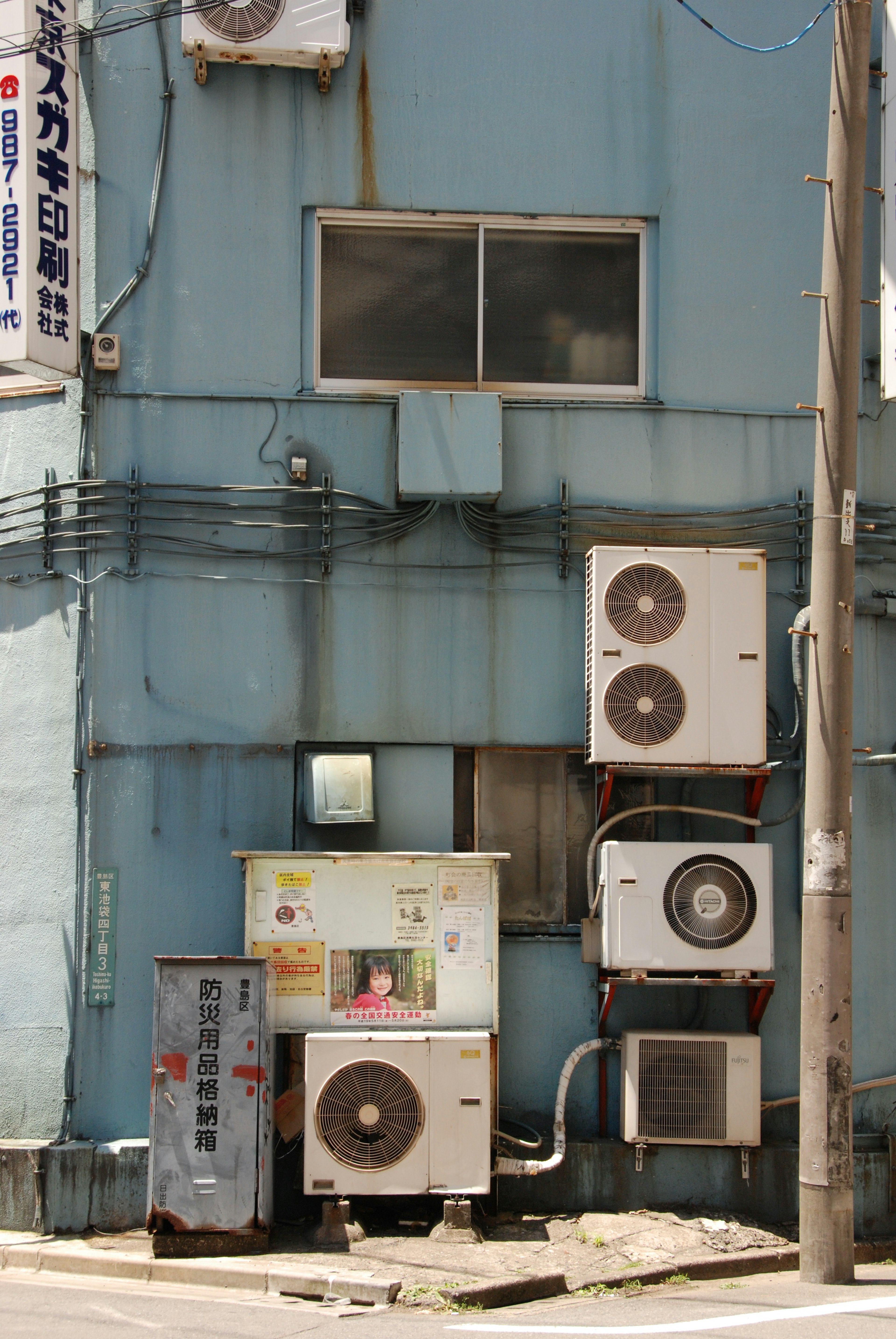 Air conditioning units mounted on a blue wall with a small window