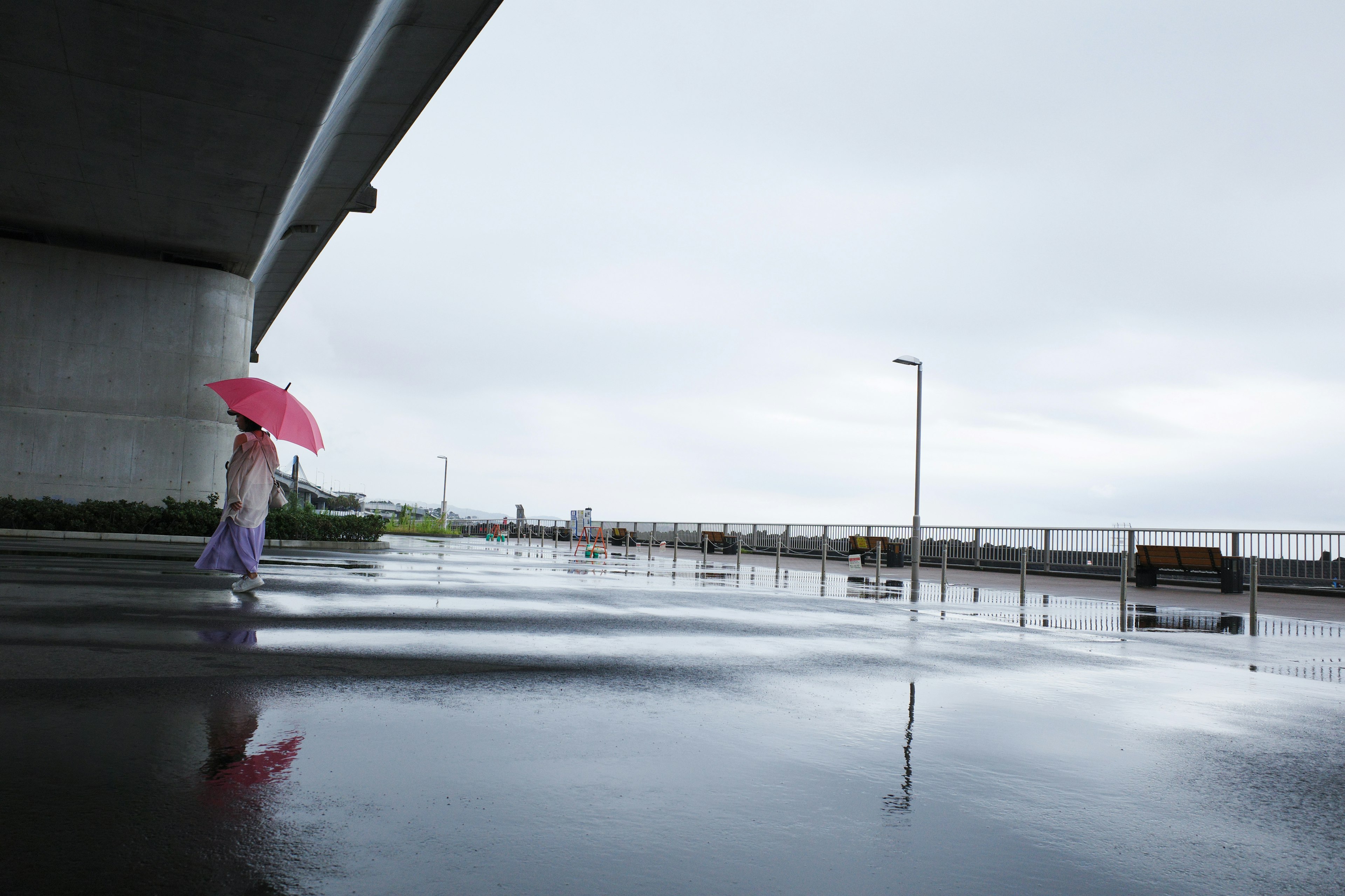 女性が赤い傘を持って歩いている雨の中の風景