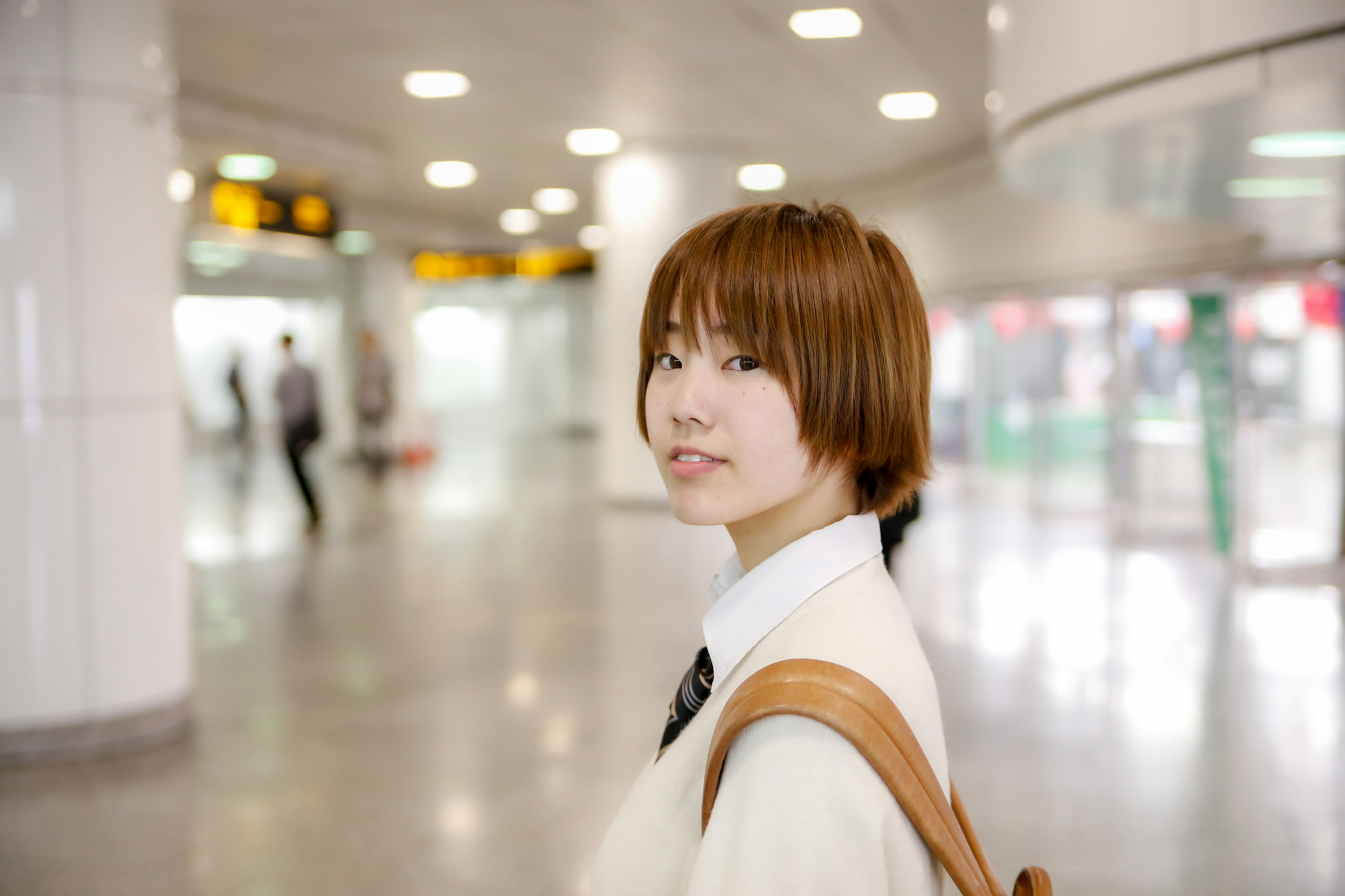 Retrato de una joven sonriendo en una estación de tren con personas y luces brillantes al fondo