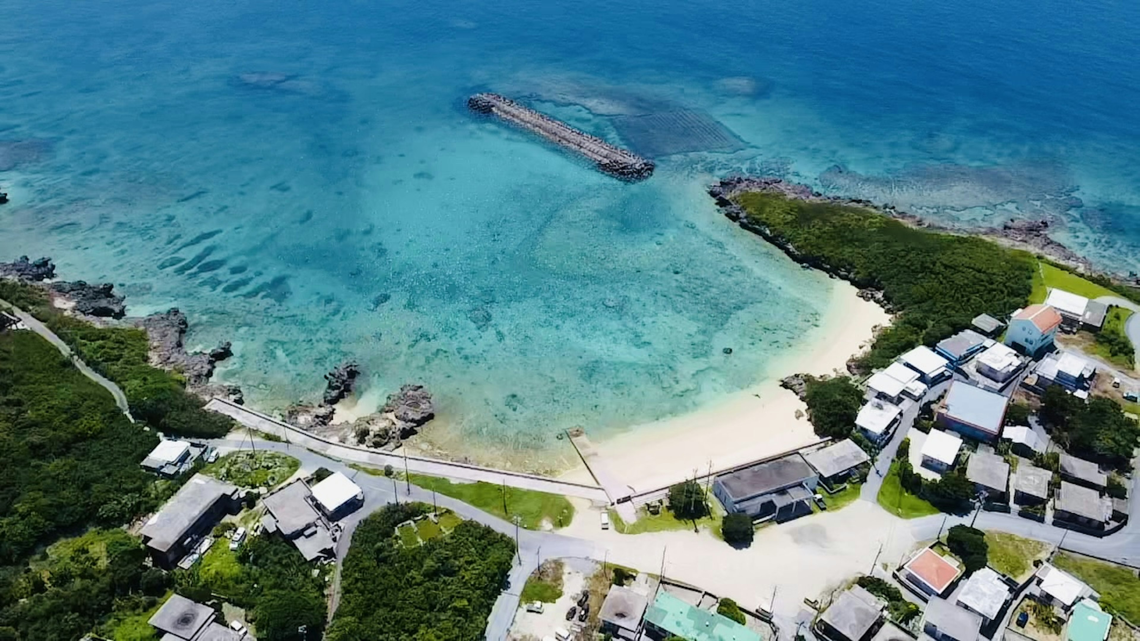 Vista aérea de un océano azul y una playa de arena con un barco atracado y casas visibles