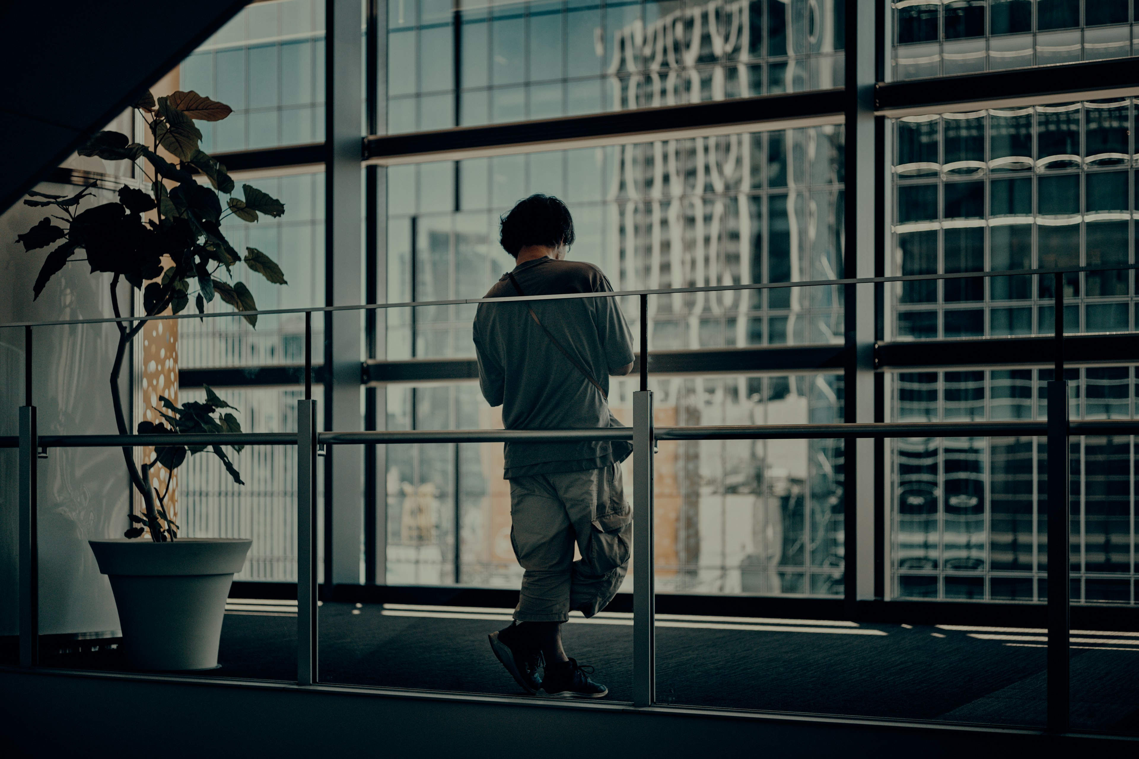 Silhouette of a young man standing by large windows in a modern office building with cityscape