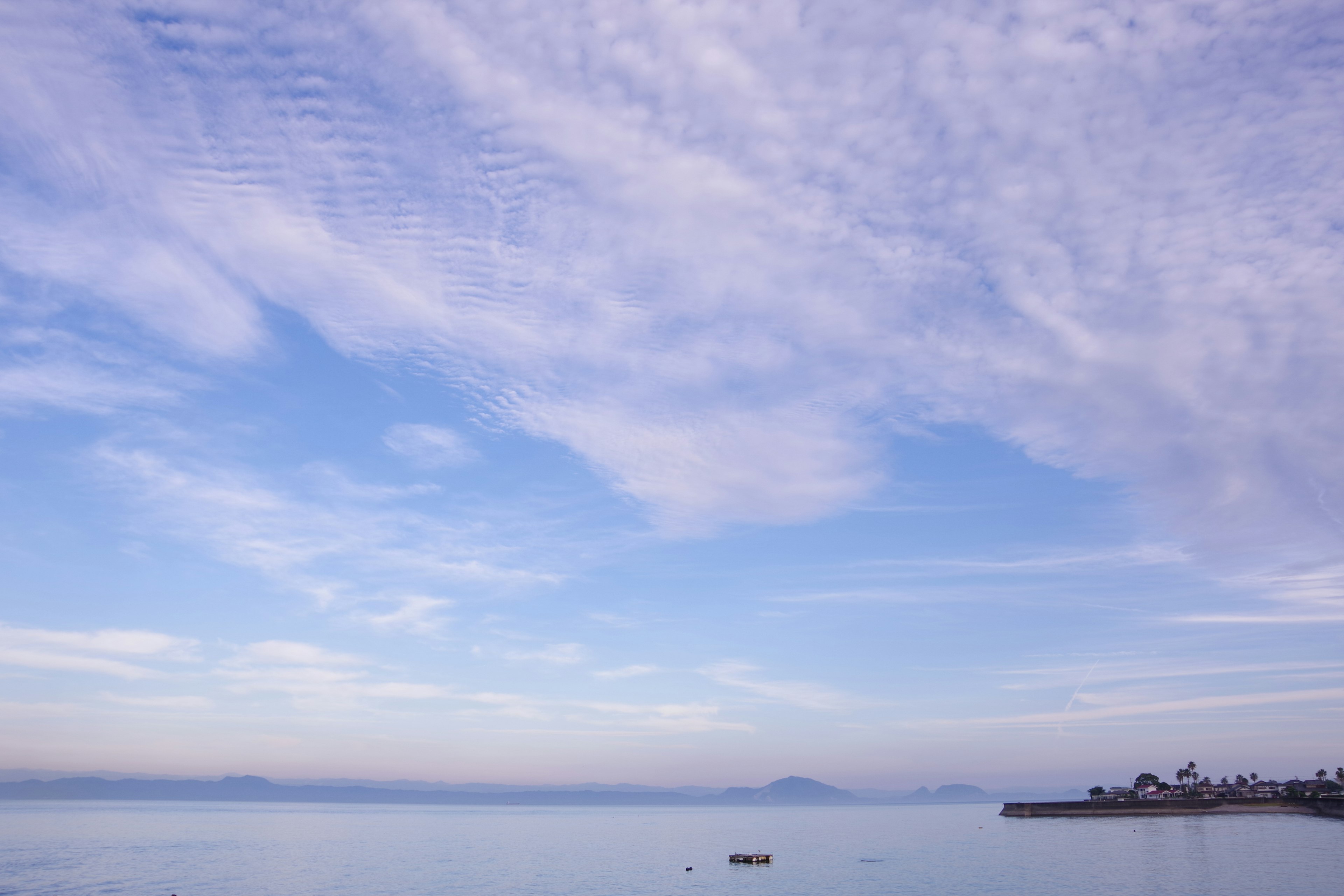 Paysage maritime serein avec ciel bleu et eau calme présentant des nuages doux