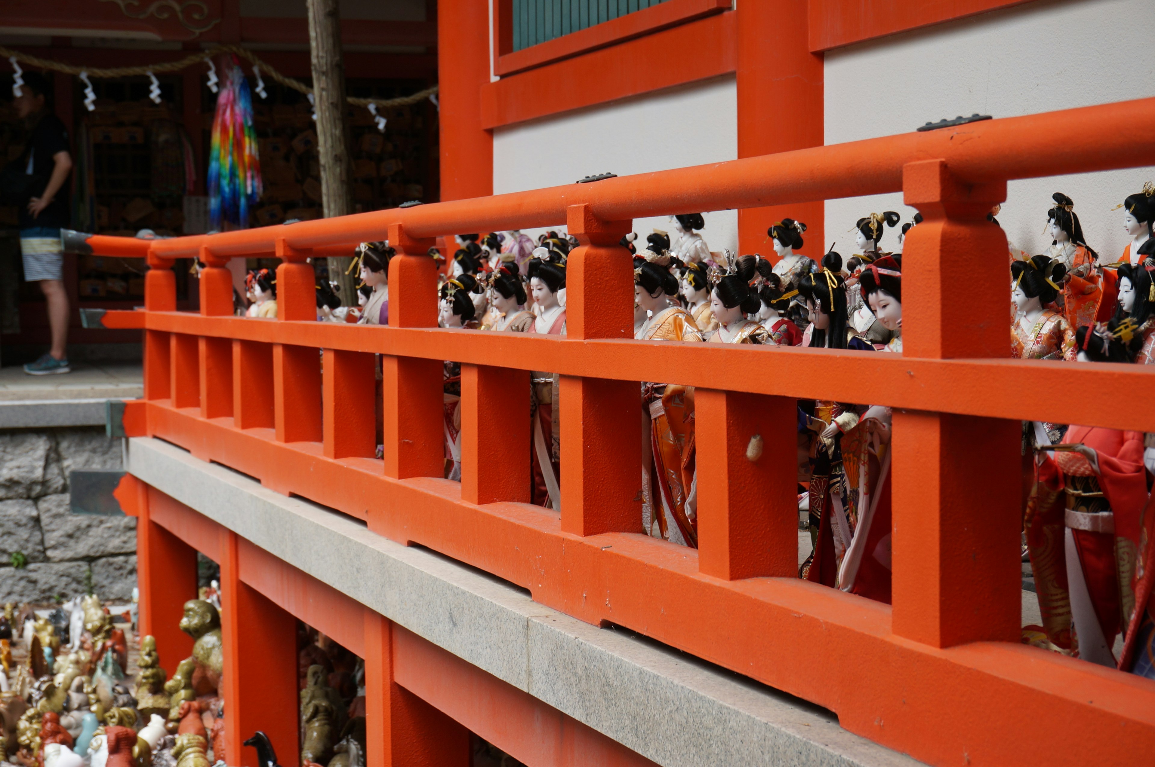 Row of dolls on a red railing with a traditional building in the background