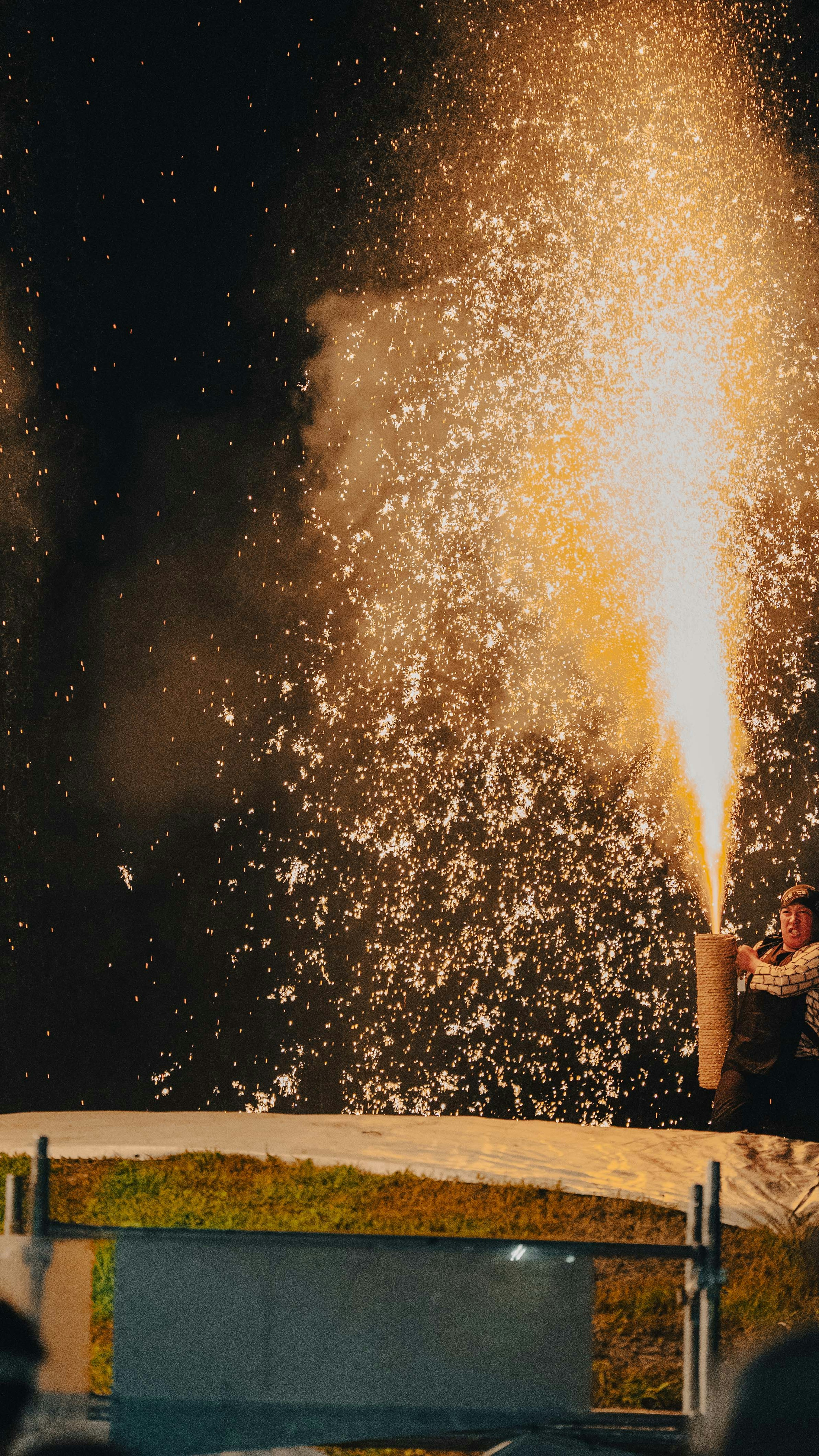 Person holding a flame thrower producing sparks in the night sky