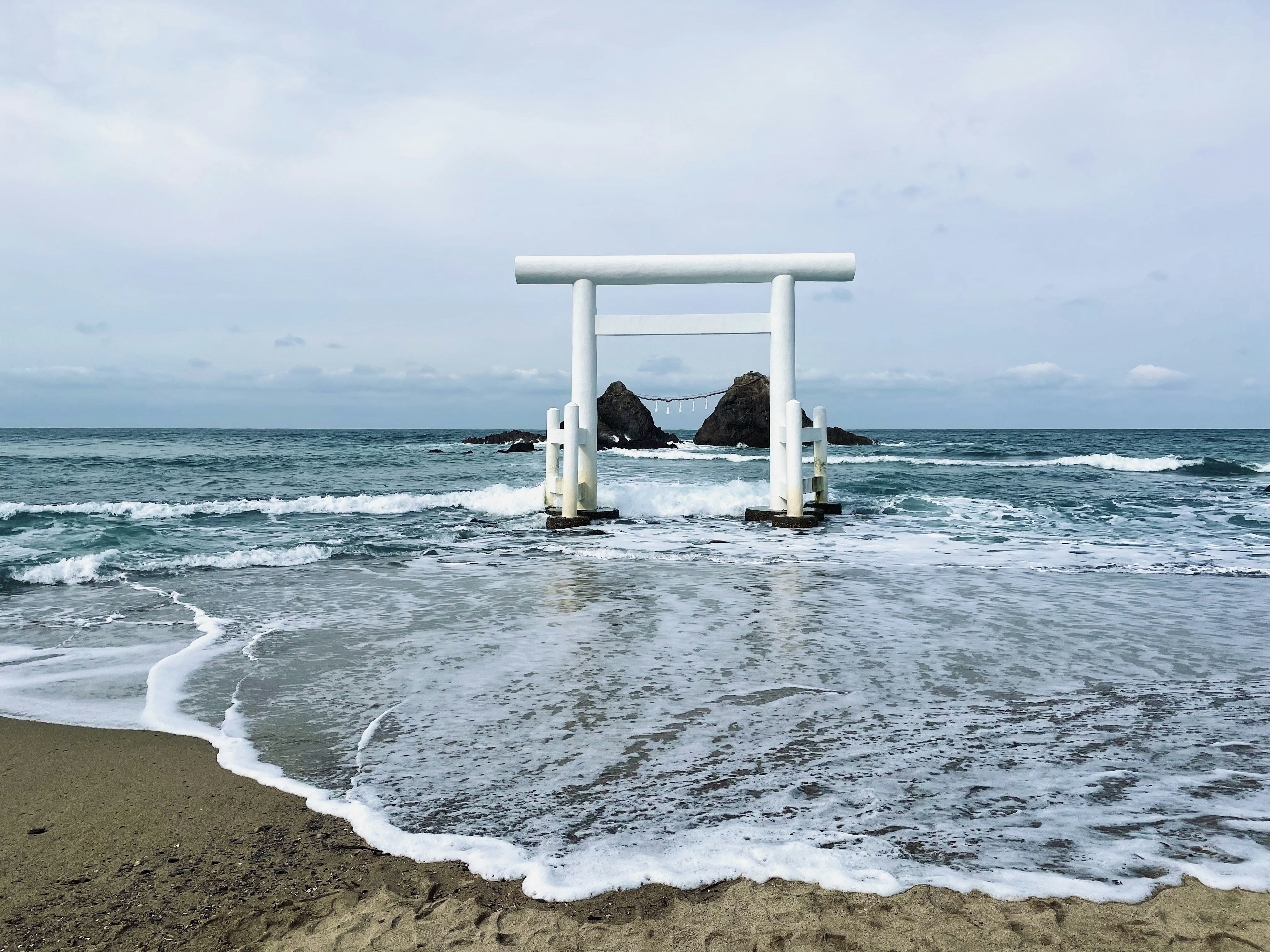 Portail torii blanc avec des vagues sur la plage