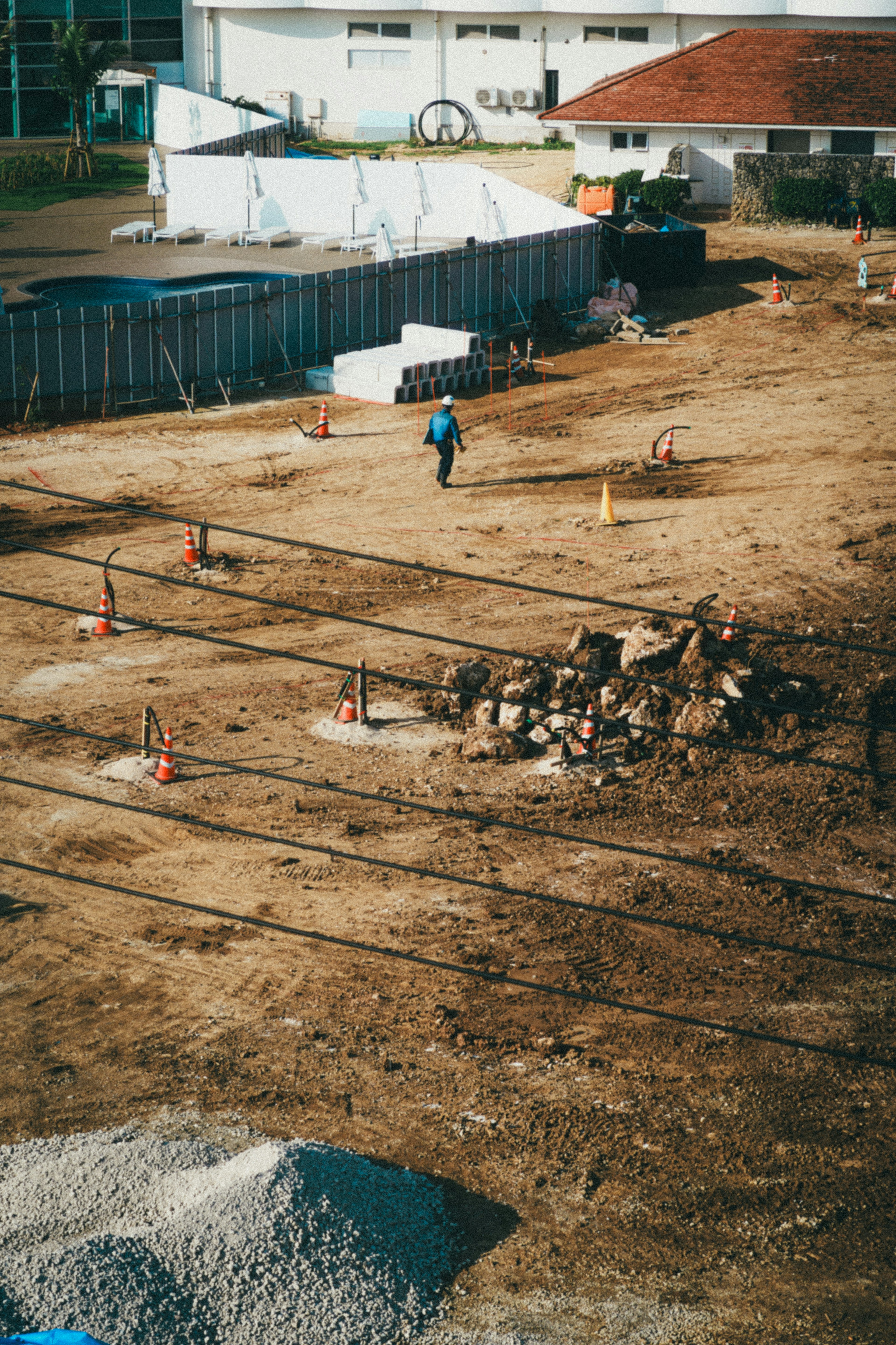 A construction site with a person walking on the ground surrounded by cones and a pile of rocks