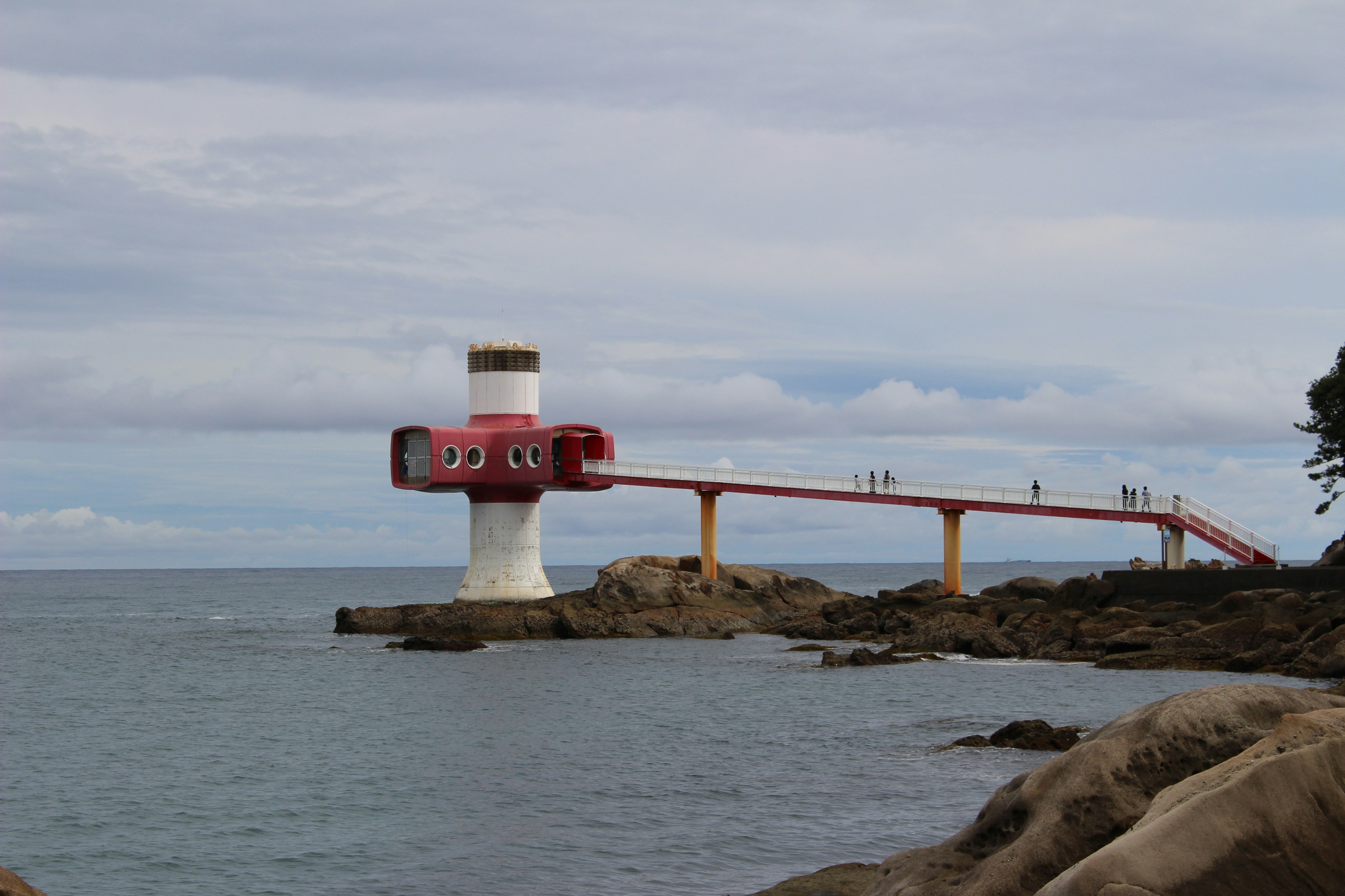 Un faro rojo único con un largo puente que se extiende hacia el mar