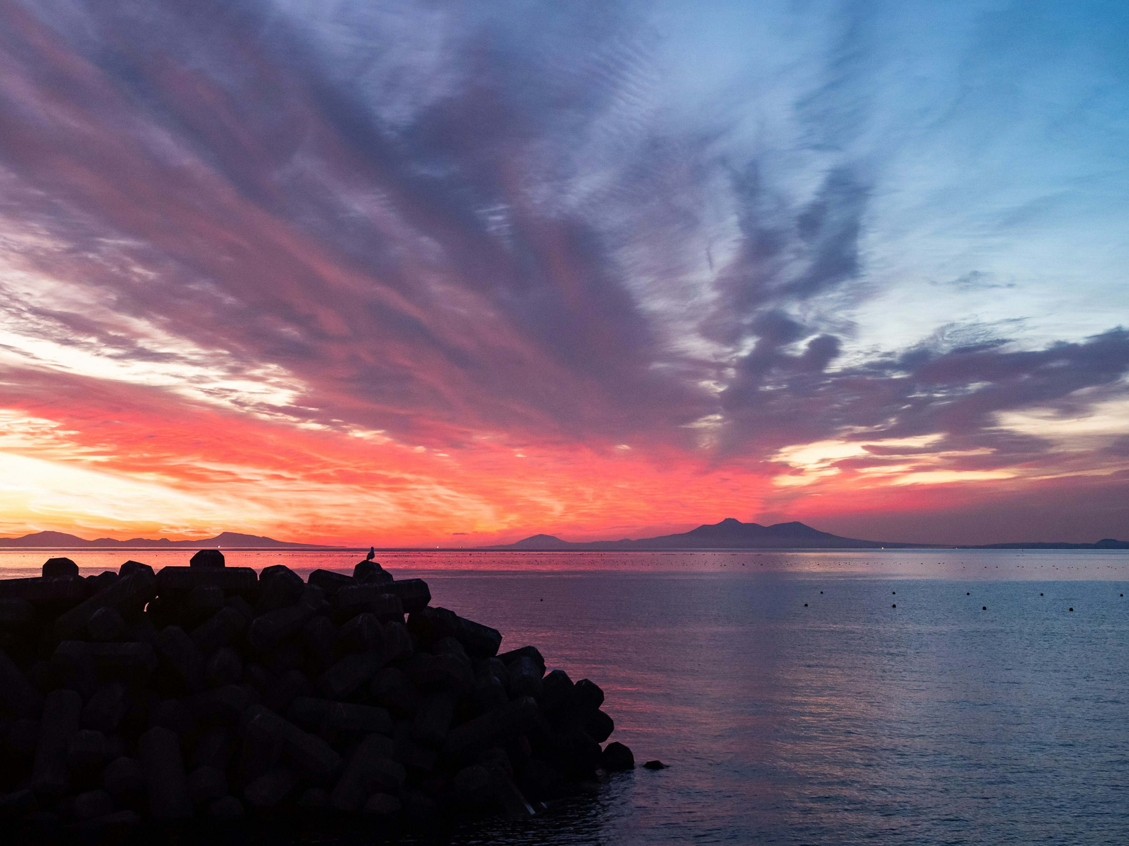 Cielo vibrante de atardecer sobre aguas tranquilas con costa rocosa y montañas distantes